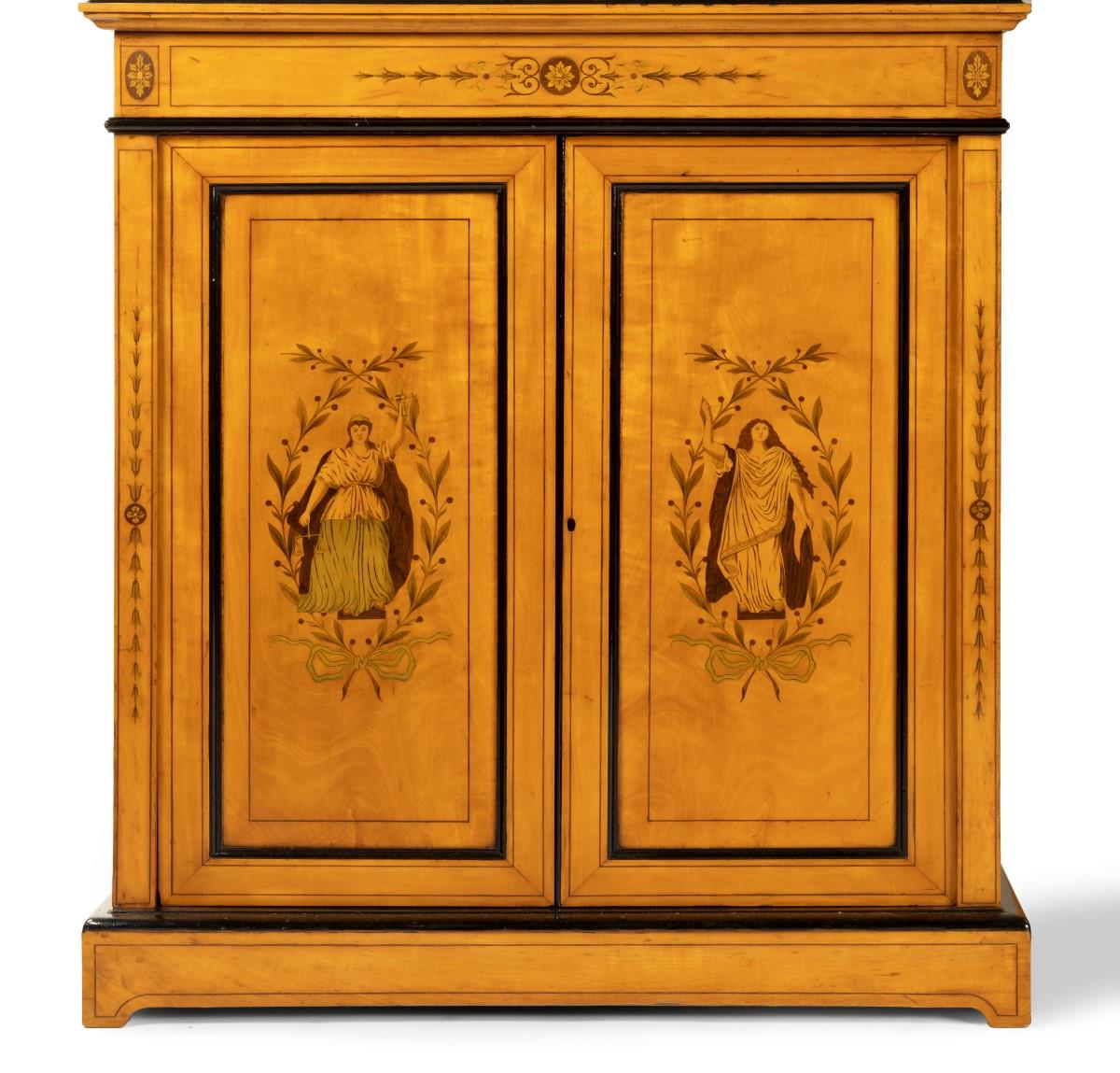 A pair of mid Victorian satinwood bookcases, each with an upper section comprising two glazed door enclosing two shelves, surmounted by a broken swan-neck pediment centred on a classical vase, all above cupboards inlaid in decorative and stained