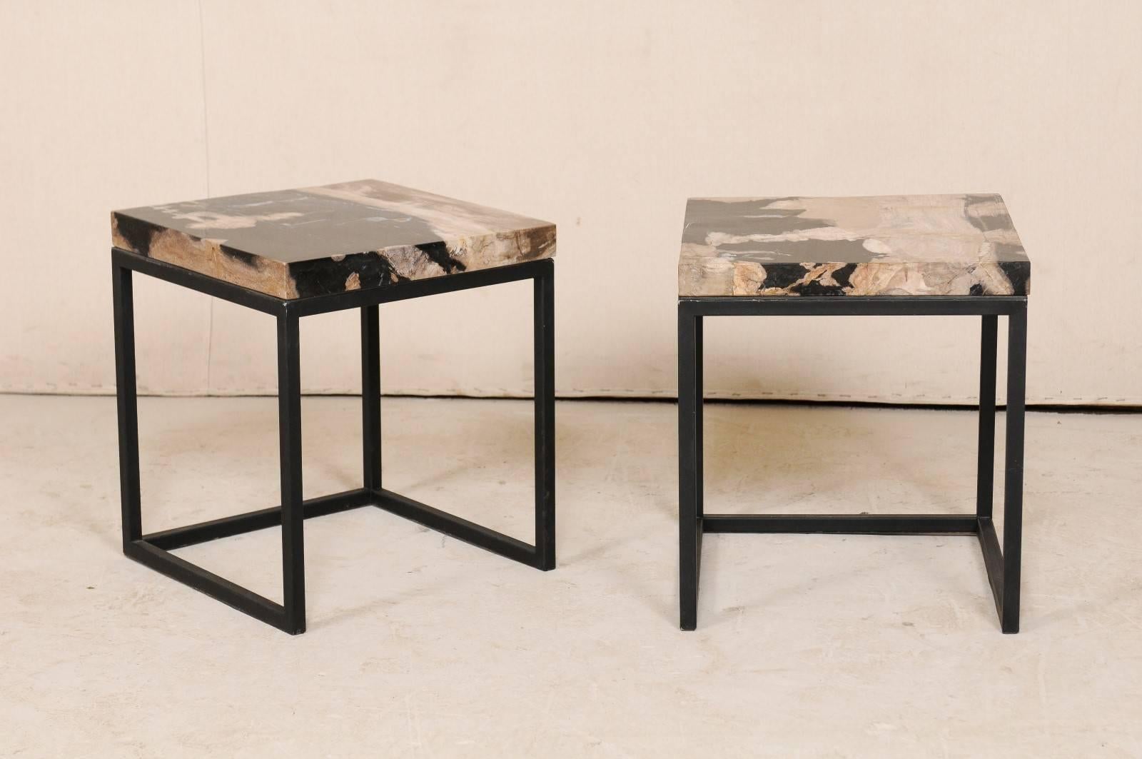 A pair of modern style custom petrified wood top drinks tables. This pair of tables each feature a square-shaped petrified wood top, with lovely black, taupe, and beige tones. The tops are supported by a custom metal base, which is black in color,