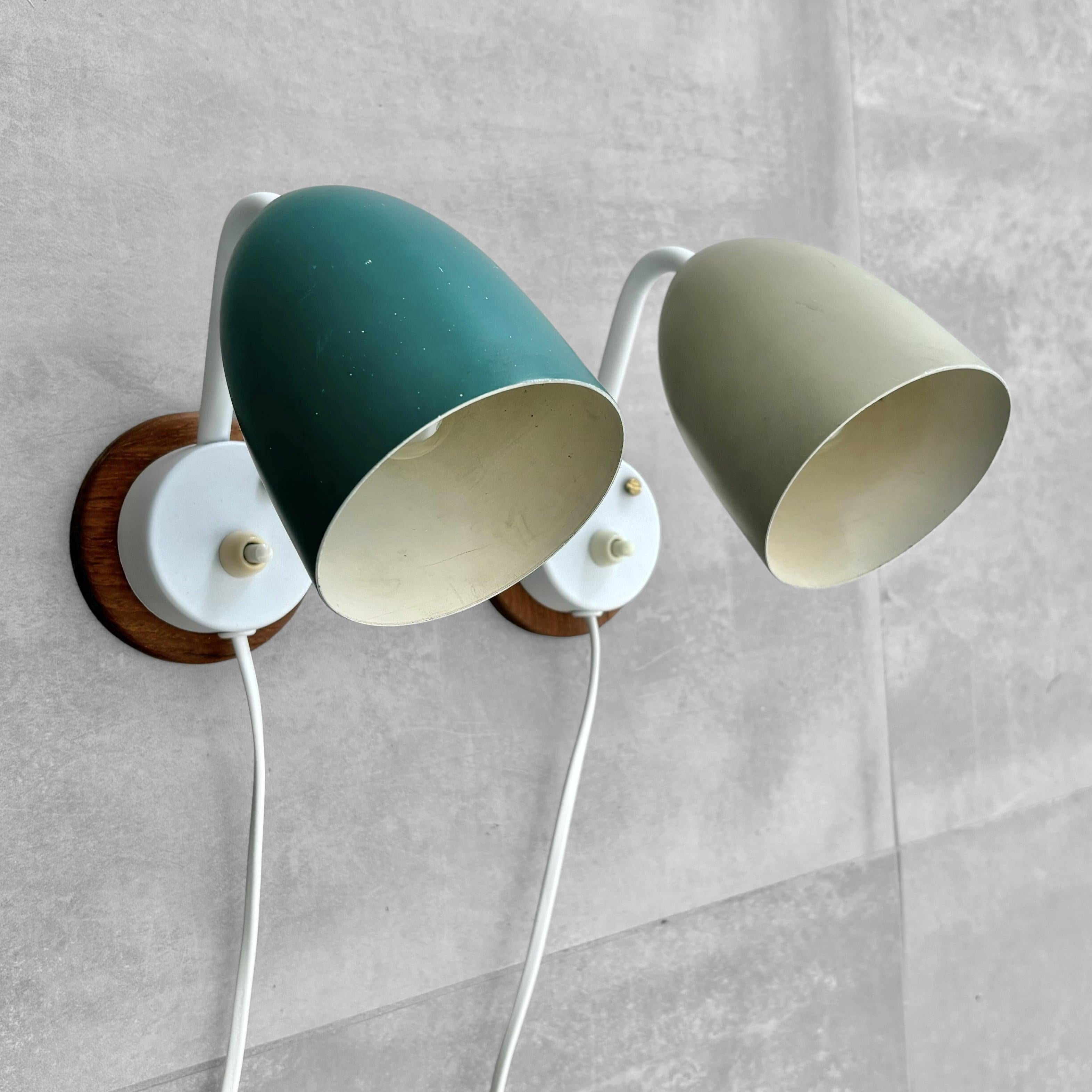 A pair of minimalist wall or bedside lamps, crafted from metal with a solid oak wall mount. They feature a luminescent light switch, making it easy to find in the dark, and a standard E14 lamp holder. Produced by an unidentified Swedish manufacturer