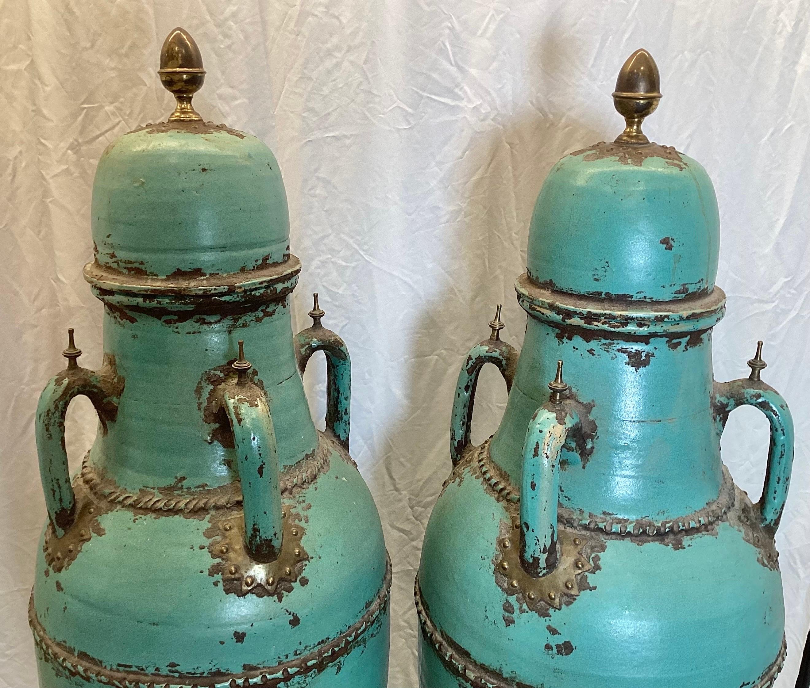 A very tall pair of Turquoise color glazed urns with lids.  These 59 inch tall potter urns with bronze mounts at the handles, and at the base with a a mottled mostly blue glazed surface.  The aged finish is intentional and original with some age