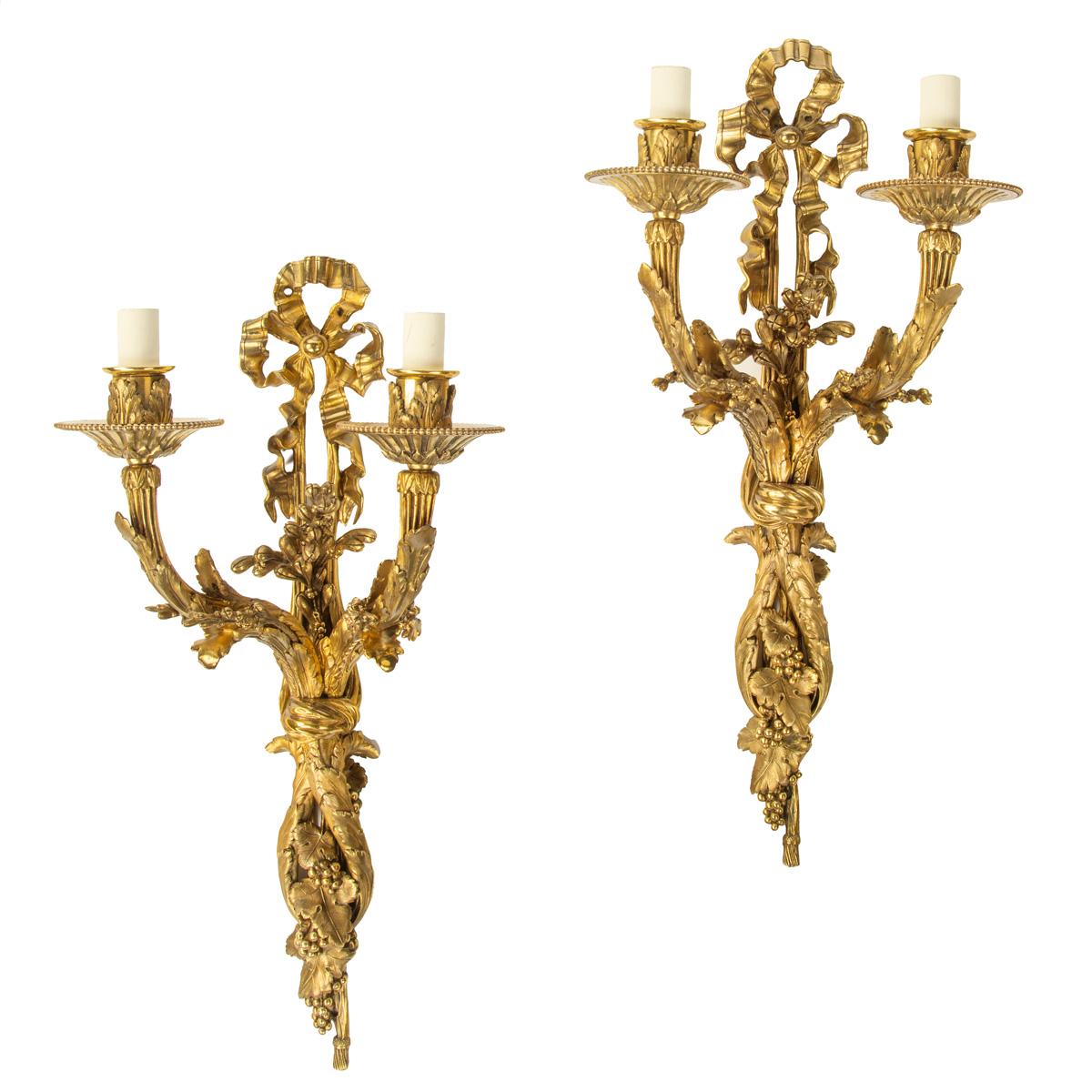 A pair of Napoleon III two-branch ormolu wall lights, each in the form of a tied ribbon supporting a stem of fruiting vines and foliage with gadrooned drip trays and acanthus carved socles, now wired for electricity. French, circa 1860.

