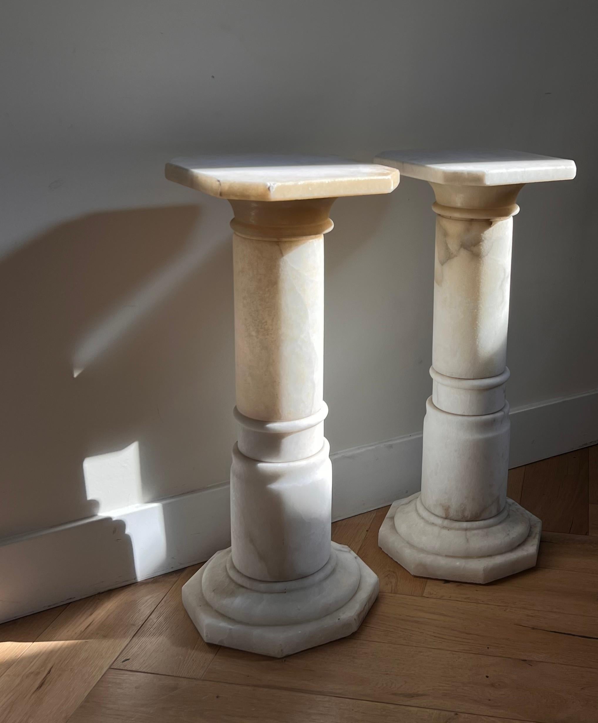 A pair of neoclassical alabaster pedestals, circa early 1960s. Cream with ash veining, they glow every so slightly translucent when the light is right. A loss on one edge and some stubborn epoxy of yore, otherwise good condition. Pick up in central