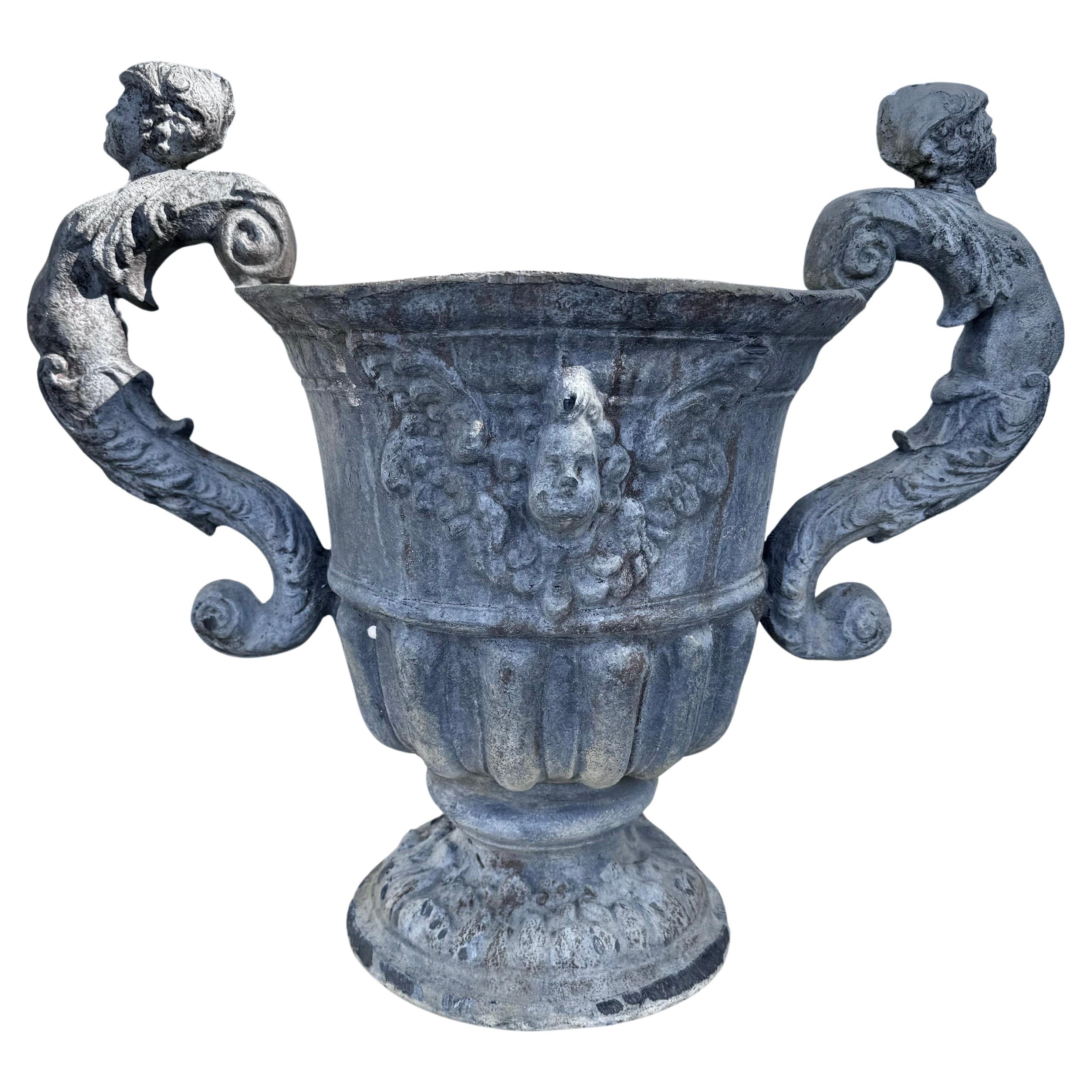 Coppia di fioriere neoclassiche a forma di urna della fine del XIX secolo con due manici figurati e putti in rilievo. Attraente patinatura grigia e rovinata dagli agenti atmosferici. Possono essere piantati o utilizzati come vasi decorativi.