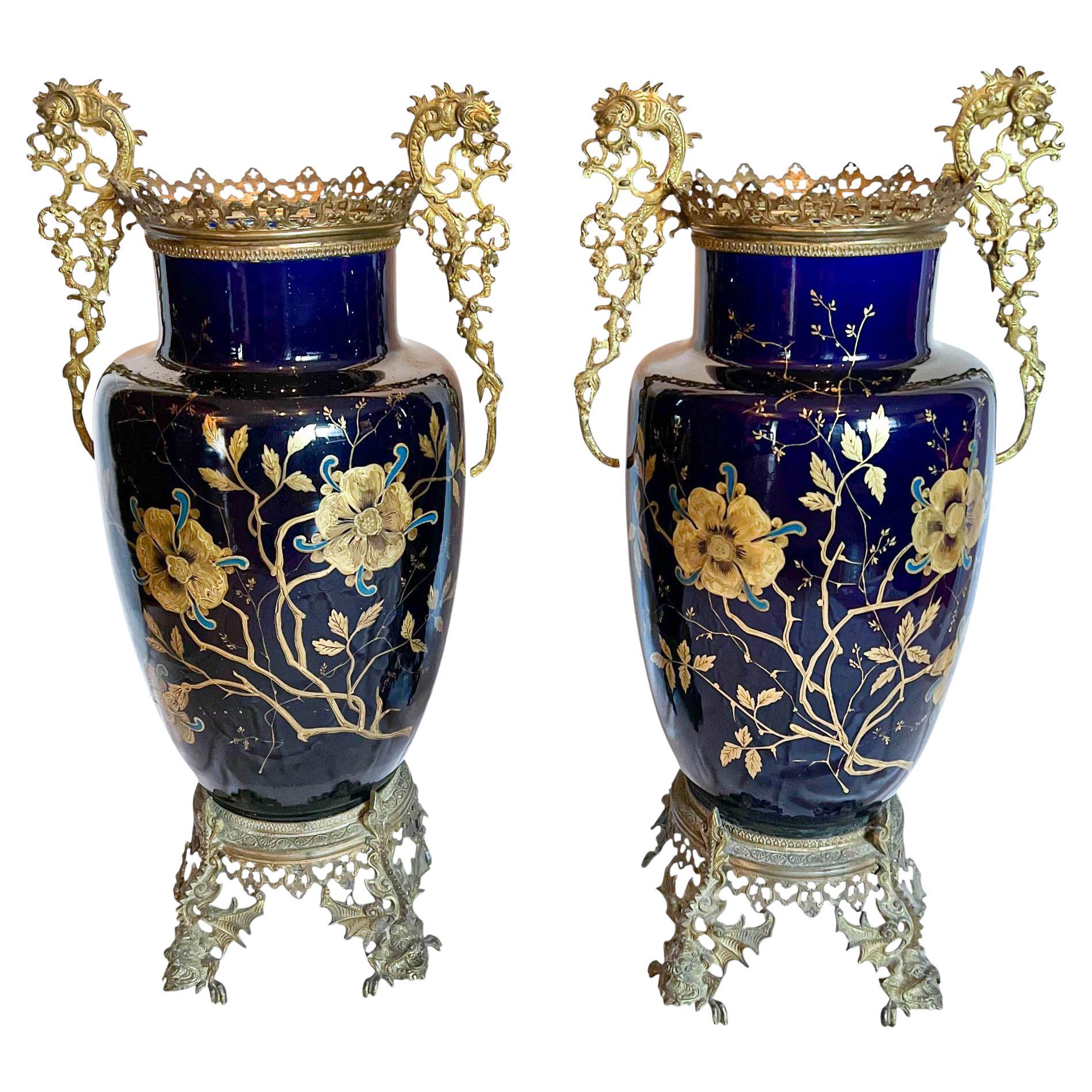 Questa coppia di vasi combina la porcellana cobalto con supporti in bronzo dorato finemente fusi e cesellati, una sintesi caratteristica dell'arte decorativa neoclassica. I corpi in porcellana sono smaltati in un profondo blu cobalto con finitura