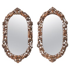 A pair of Northern European carved walnut oval panel mounts adapted as mirrors