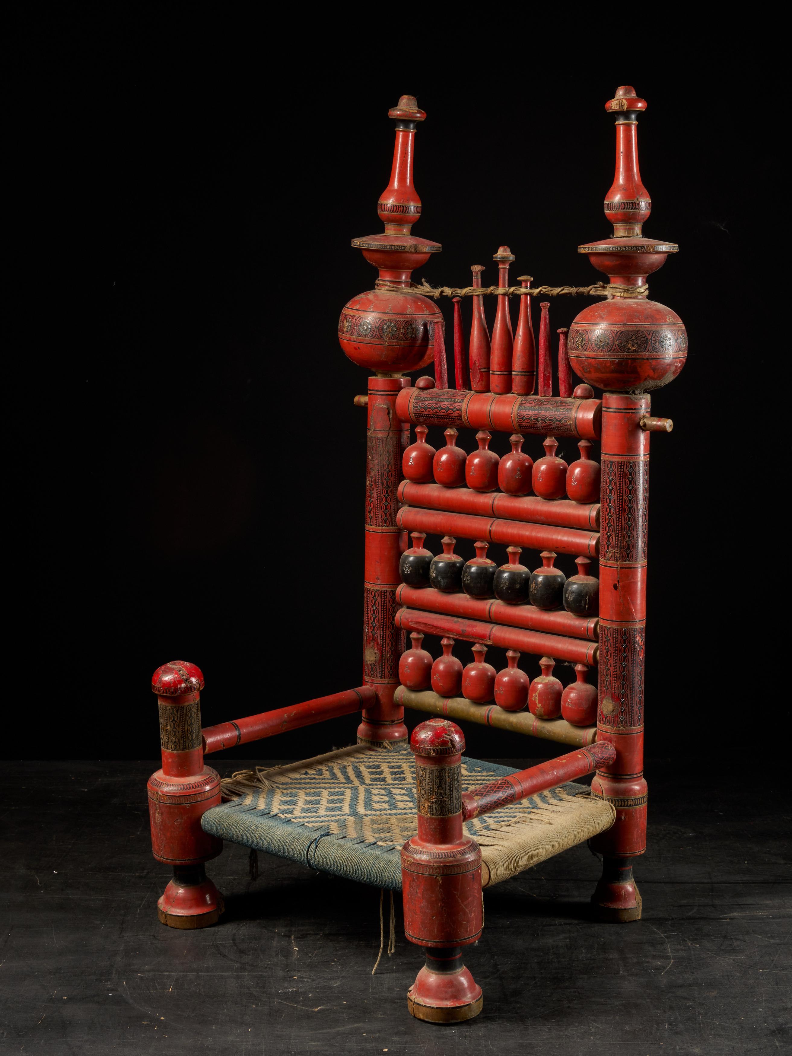 A pair of old Punjabi handcrafted wooden tribal wedding chairs with intricate woven rope seating. The chairs are hand painted in vibrant reds and blacks slightly fading. The minor losses and the wonderful gently worn patina commensurate with its age