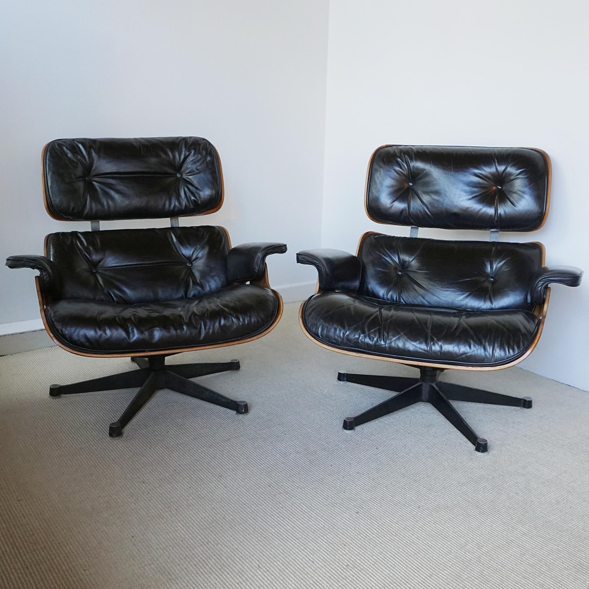 A pair of Eames chairs model 670 and Ottoman 671 manufactured under license in the UK by the Hille Furniture Company between 1957-1967. Walnut veneered with original black leather upholstery. Herman Miller Hille makers label to chairs and ottoman .