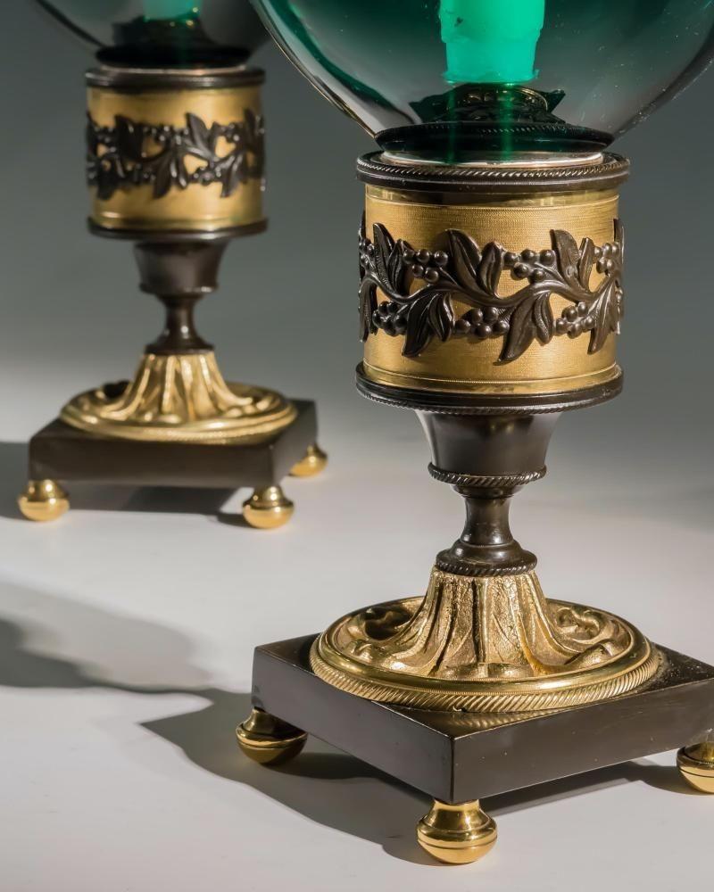 A fine pair of ormolu and bronze bases mounted on semi ball feet with finely knurled bodies incasing flowering vine bands mounting peacock green storm shades engraved with corresponding flowering vines.