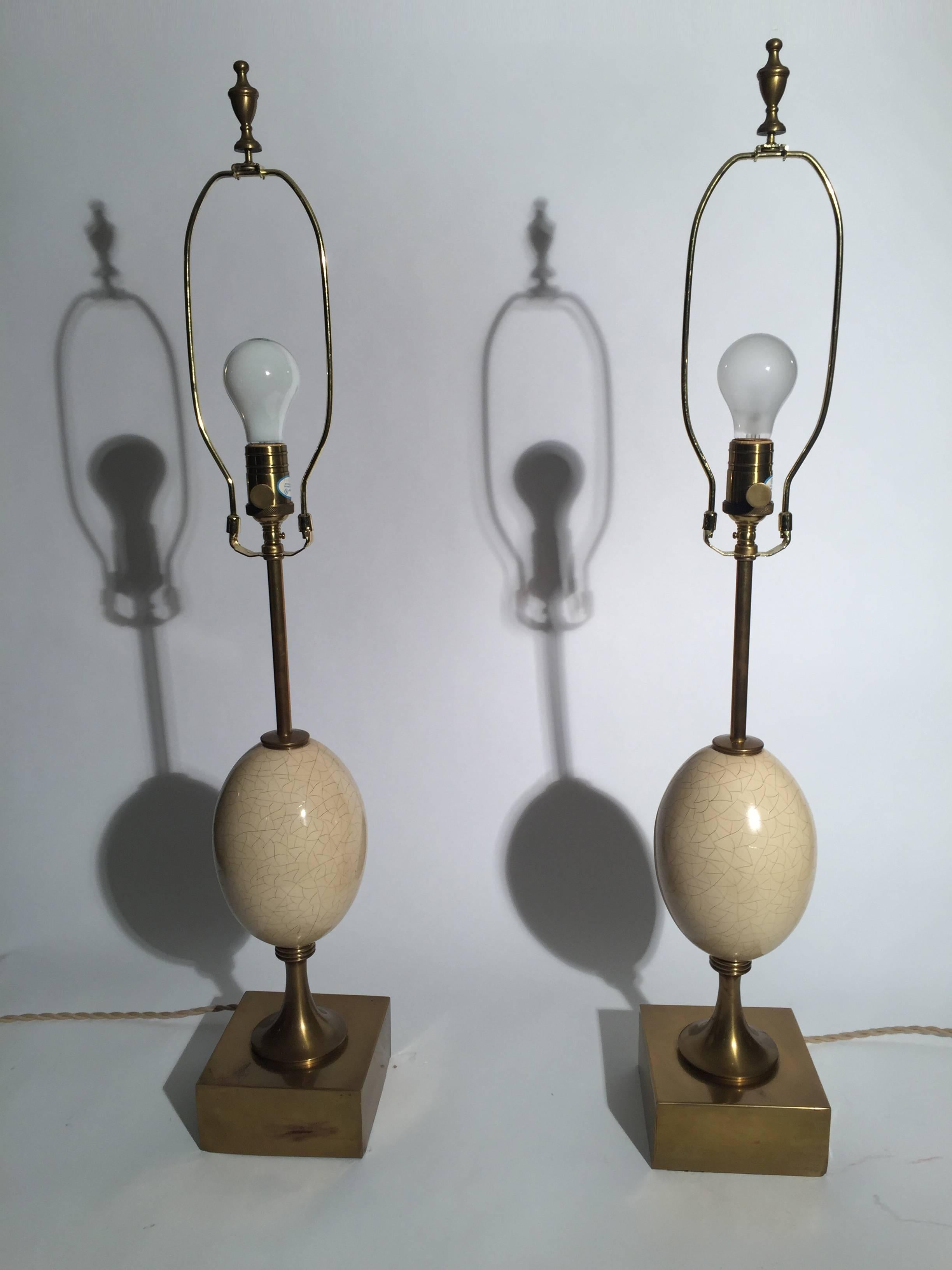 A pair of burnished brass and enamel Mid-Century Modern lamps in the form of Ostrich eggs. The eggs are metal with a crackle enamel resembling the crackle finish of an ostrich egg. Very chic and stylish. The simple drum shades are for photographic