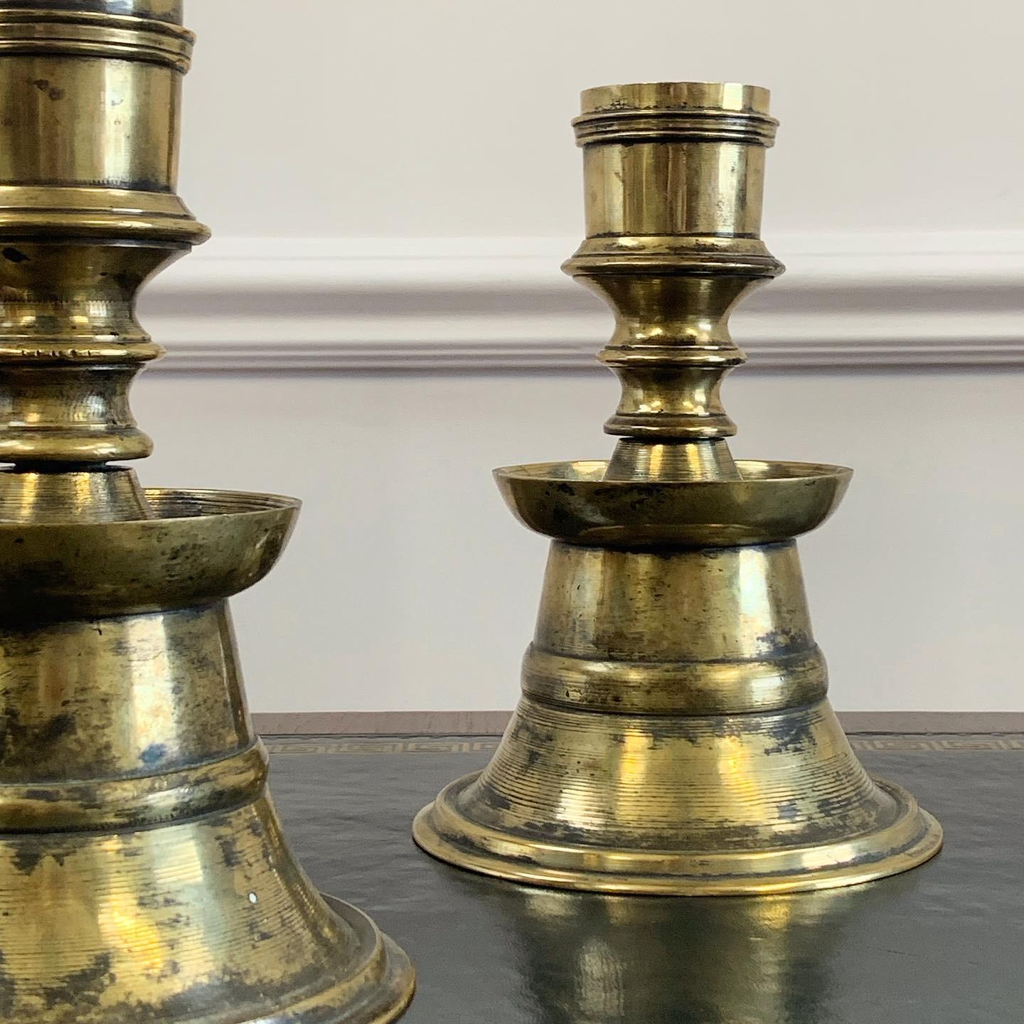 A pair of heavy gauge brass ottoman candlesticks, the lower section with flaring banded skirt narrowing to the waist and flaring out to the circular section rim, the upper section with tubular neck and a flaring banded truncated conical mouth