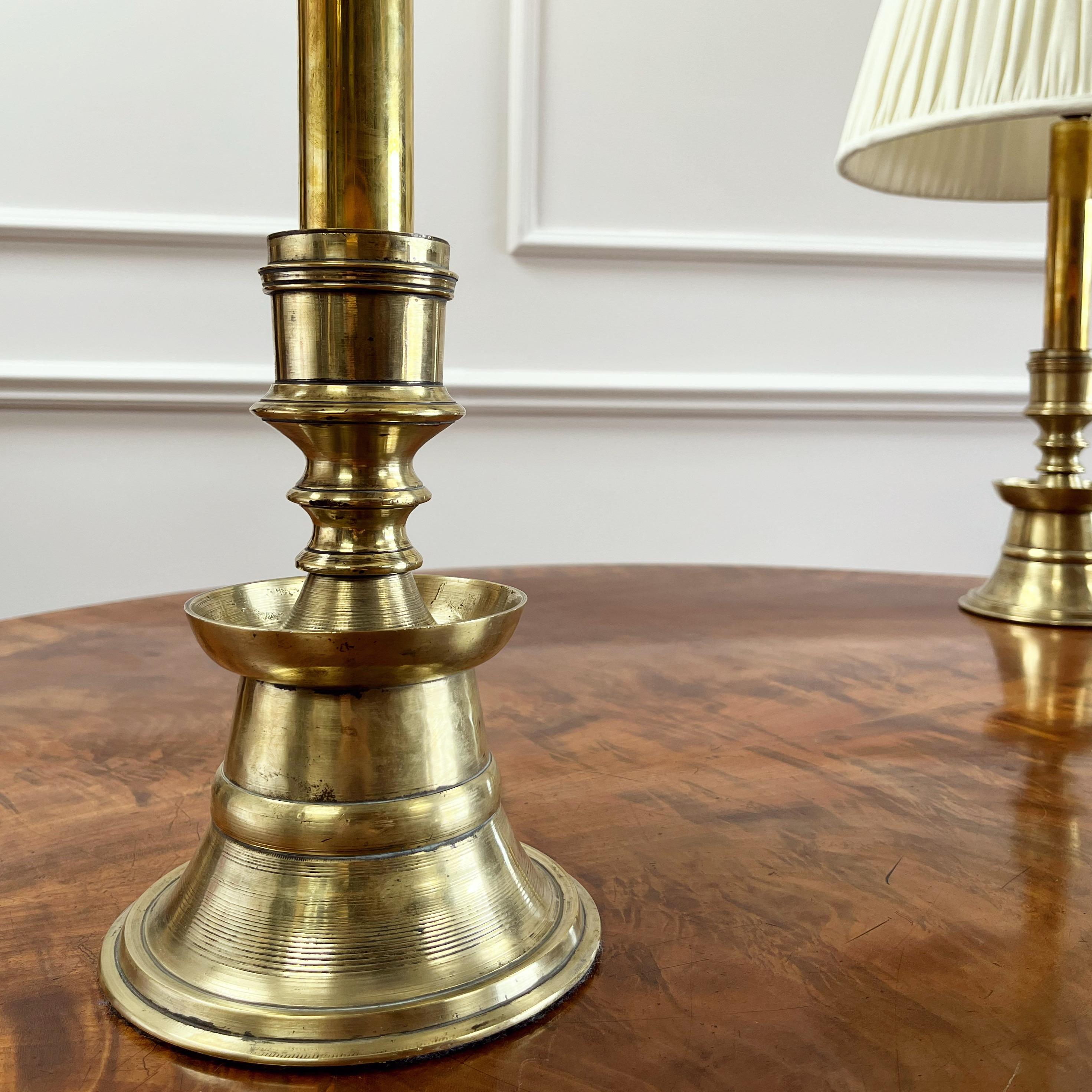 A pair of heavy gauge brass ottoman candlesticks, the lower section with flaring banded skirt narrowing to the waist and flaring out to the circular section rim, the upper section with tubular neck and a flaring banded truncated conical mouth