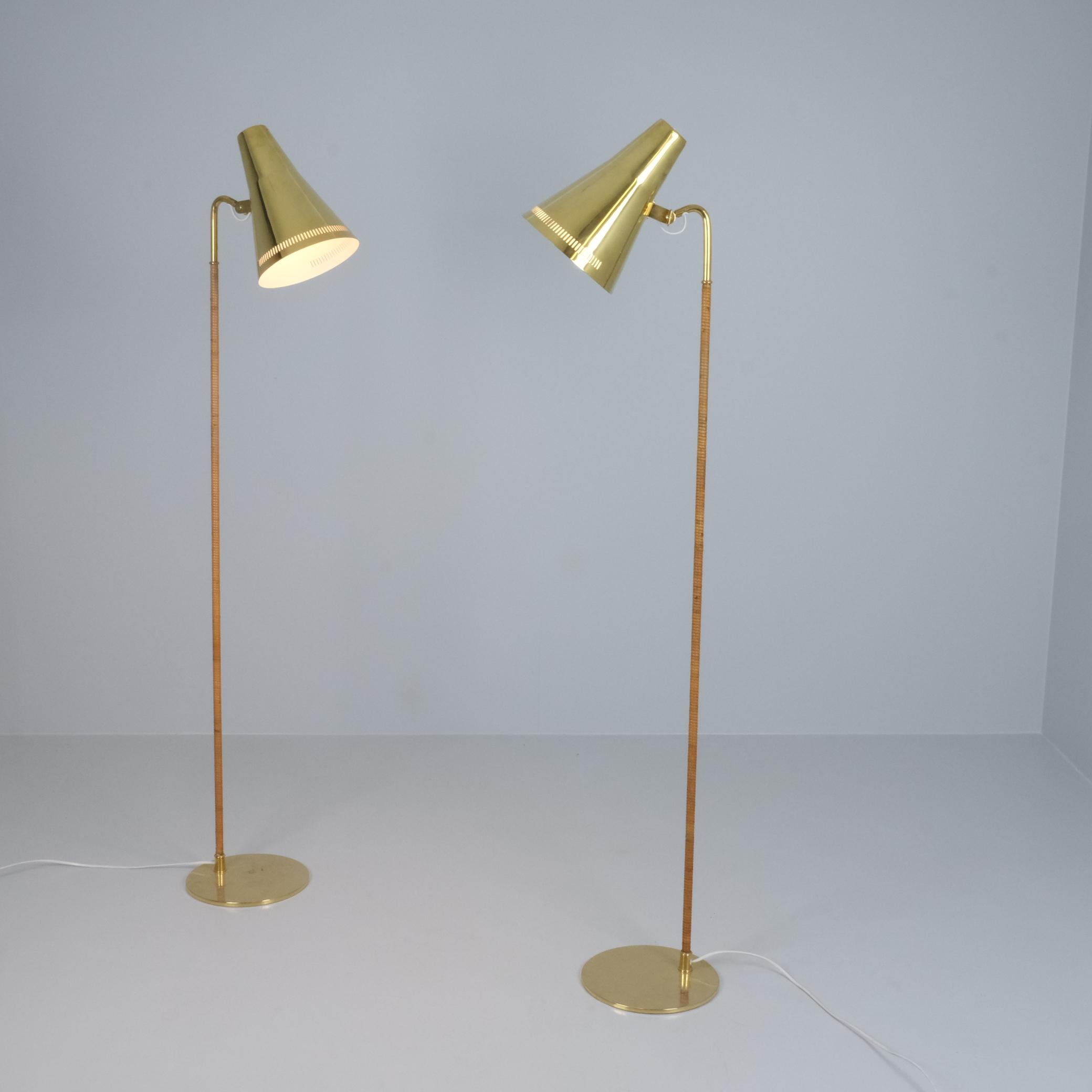 Una coppia di lampade da terra graziosamente sottili con un paralume in ottone massiccio e uno stelo avvolto in rattan. Queste lampade combinano armoniosamente la freddezza dell'ottone e il calore naturale del rattan per creare un design in grado di