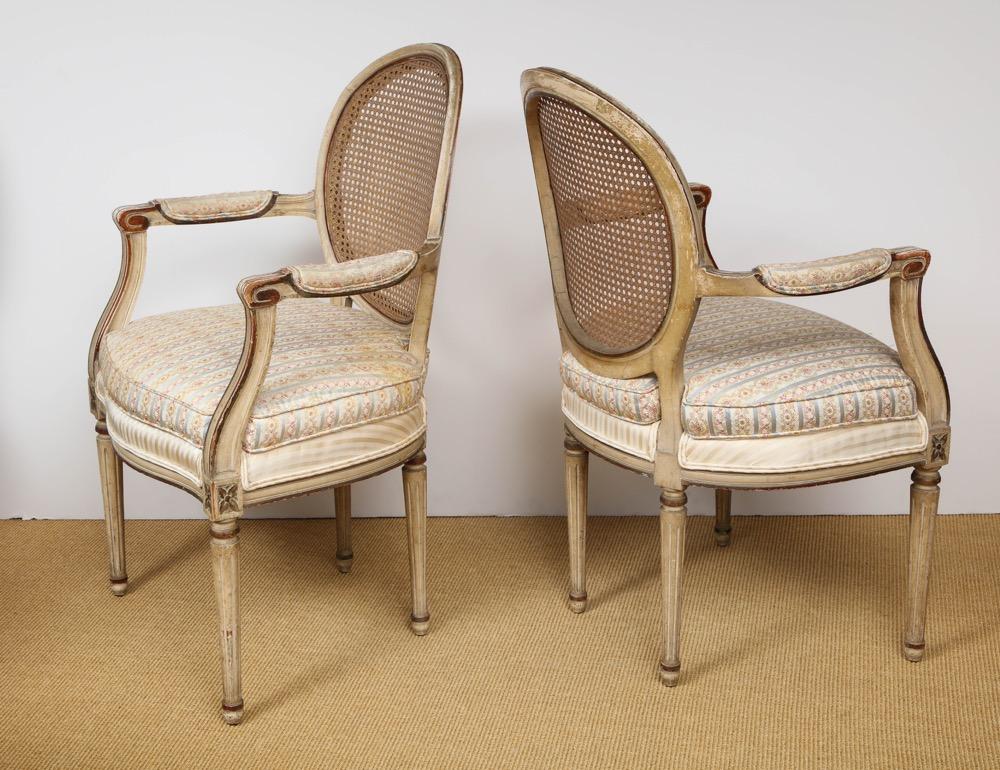 Paire de fauteuils Louis XVI à dossier rond mouluré et cannelé, avec des accoudoirs similaires étirés, assise rembourrée sur des pieds tournés et cannelés. Attribué à la Maison Jansen
