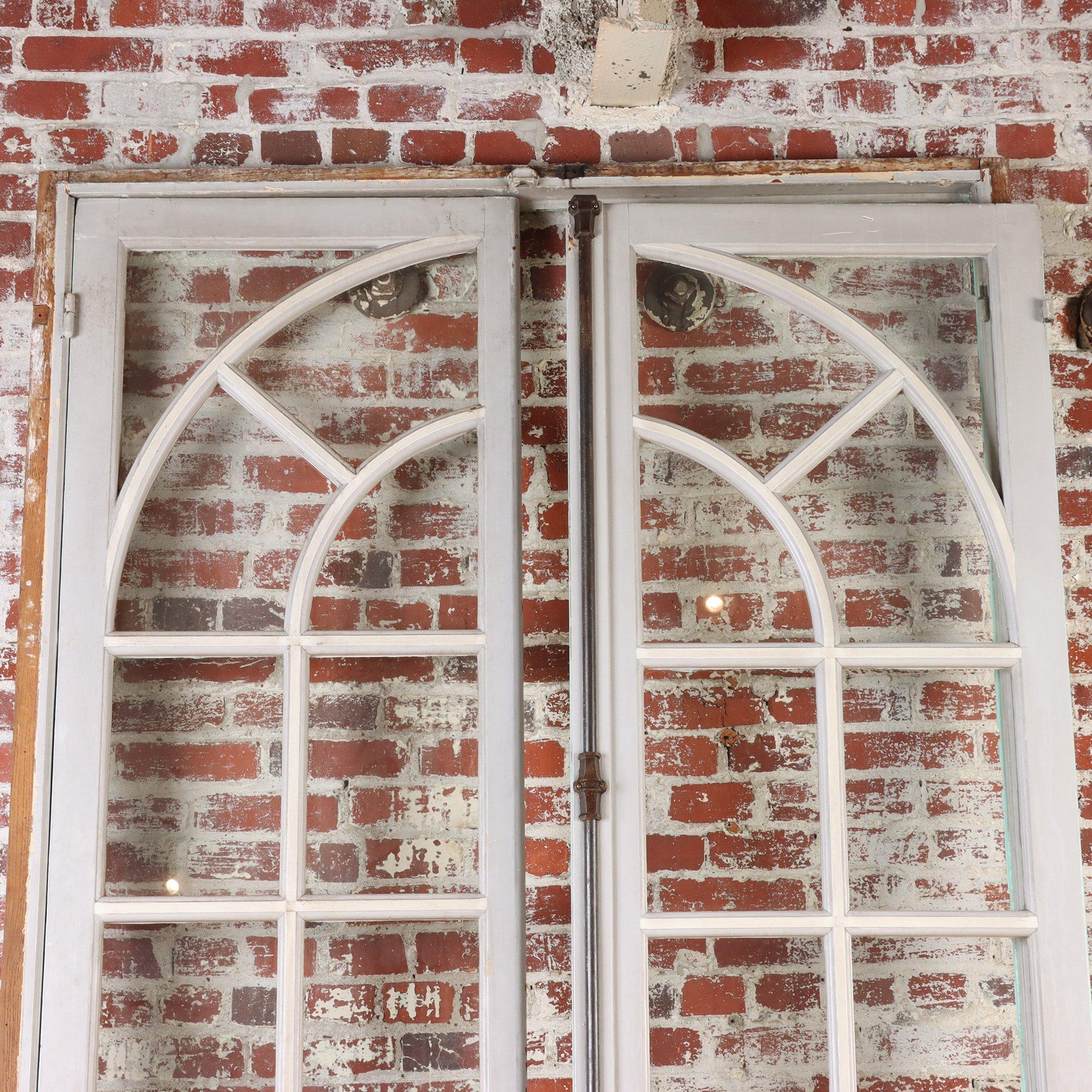 A pair of painted French doors with individual panes featuring an arched design. The doors have their original iron hardware. C 1900. Two pair are available.