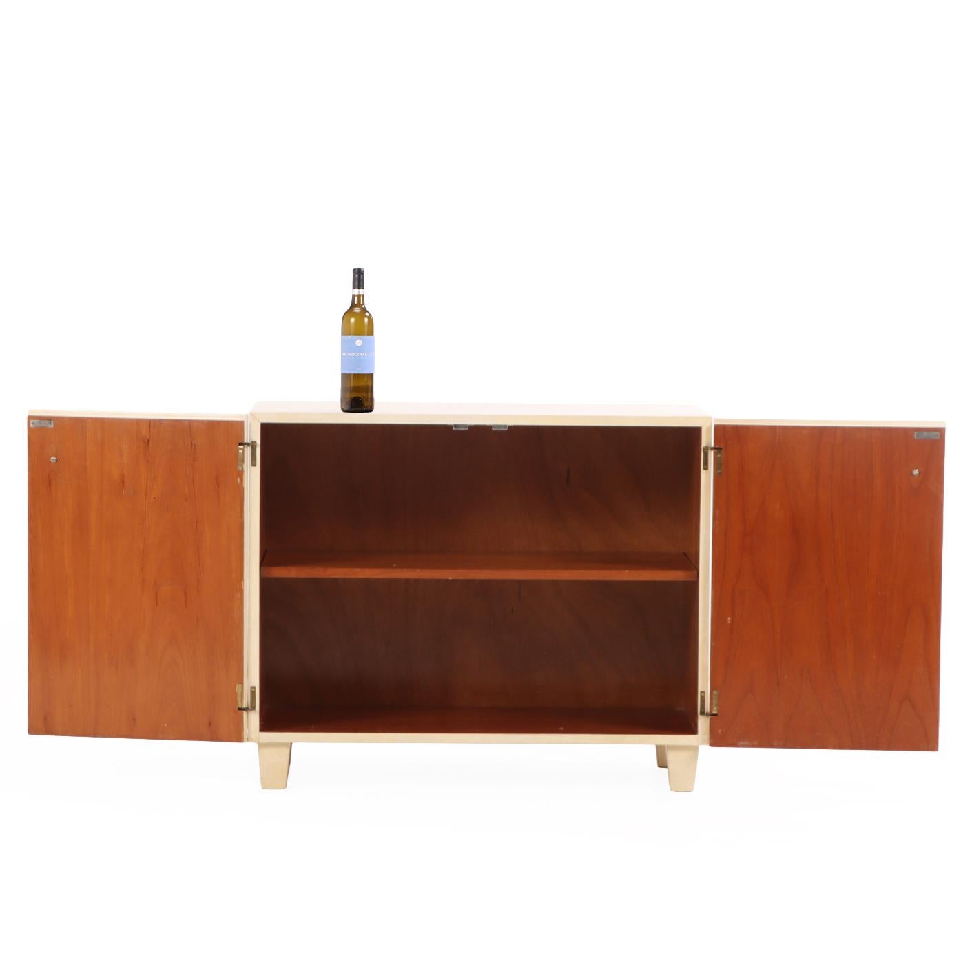 A refined pair of mid-century modern cabinets, each fully wrapped in natural parchment (pergamino) with a soft, matte sheen that subtly enhances their clean, architectural lines. The minimalist form is balanced by understated brass ring hardware,