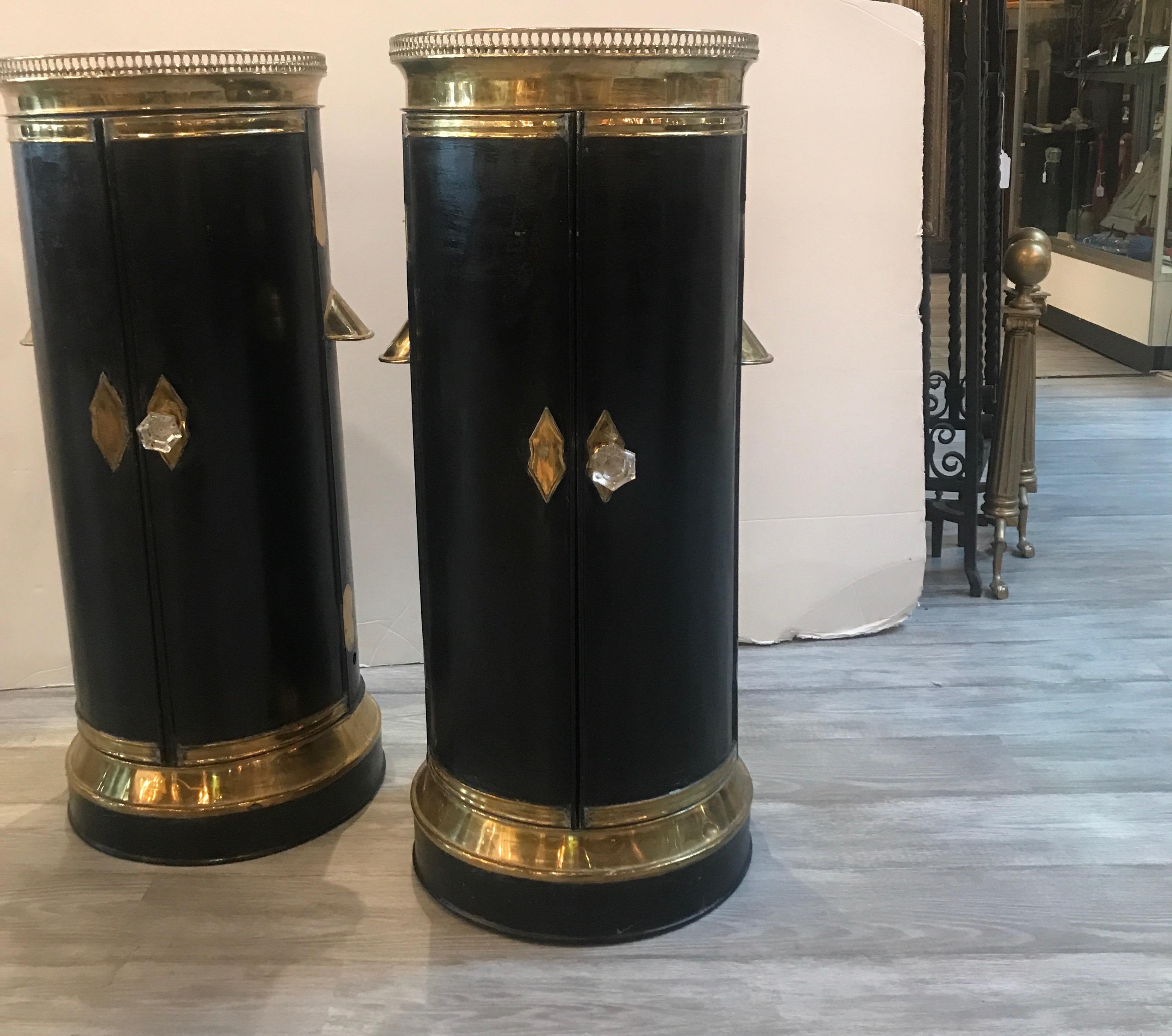 An antique pair of 19th century tole and brass round pedestal plate warmers with doors. The black painted tole ware with brass mounts and gallery edge top with two doors that open to reveal a storage area with shelf. These have age appropriate wear