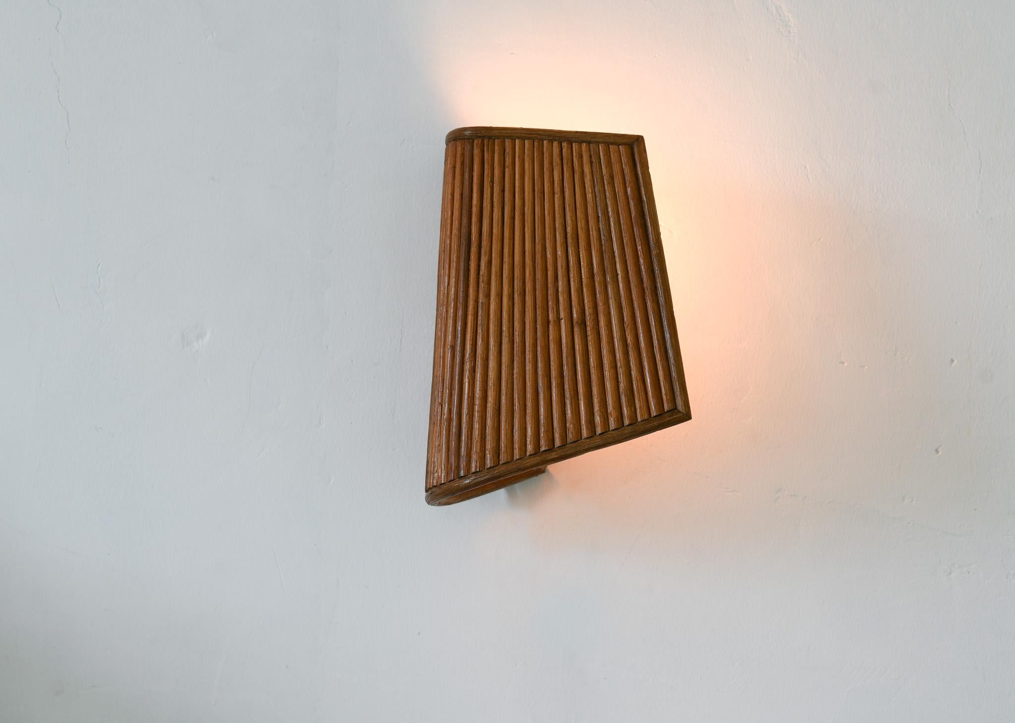 This wall mounted lamp combines modern functionality with a sculptural rattan design inspired by Italian mid-century art. The intricate rattan details and a pattern of vertical lines gives the shade an elegant vibe and unique texture. Crafted with