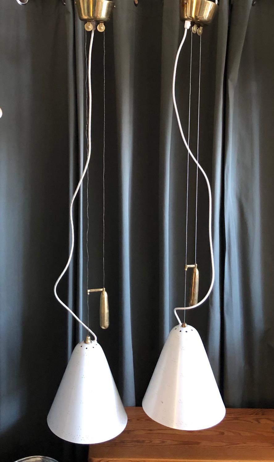 A pair of counterweight adjustable ceiling lamps, designed by Paavo Tynell for Idman. Model 1942. Painted perforated aluminum shades with polished brass counterweight details. Marked Idman. 
The shade dimensions: 11' height; 10' diameter. Drop 47