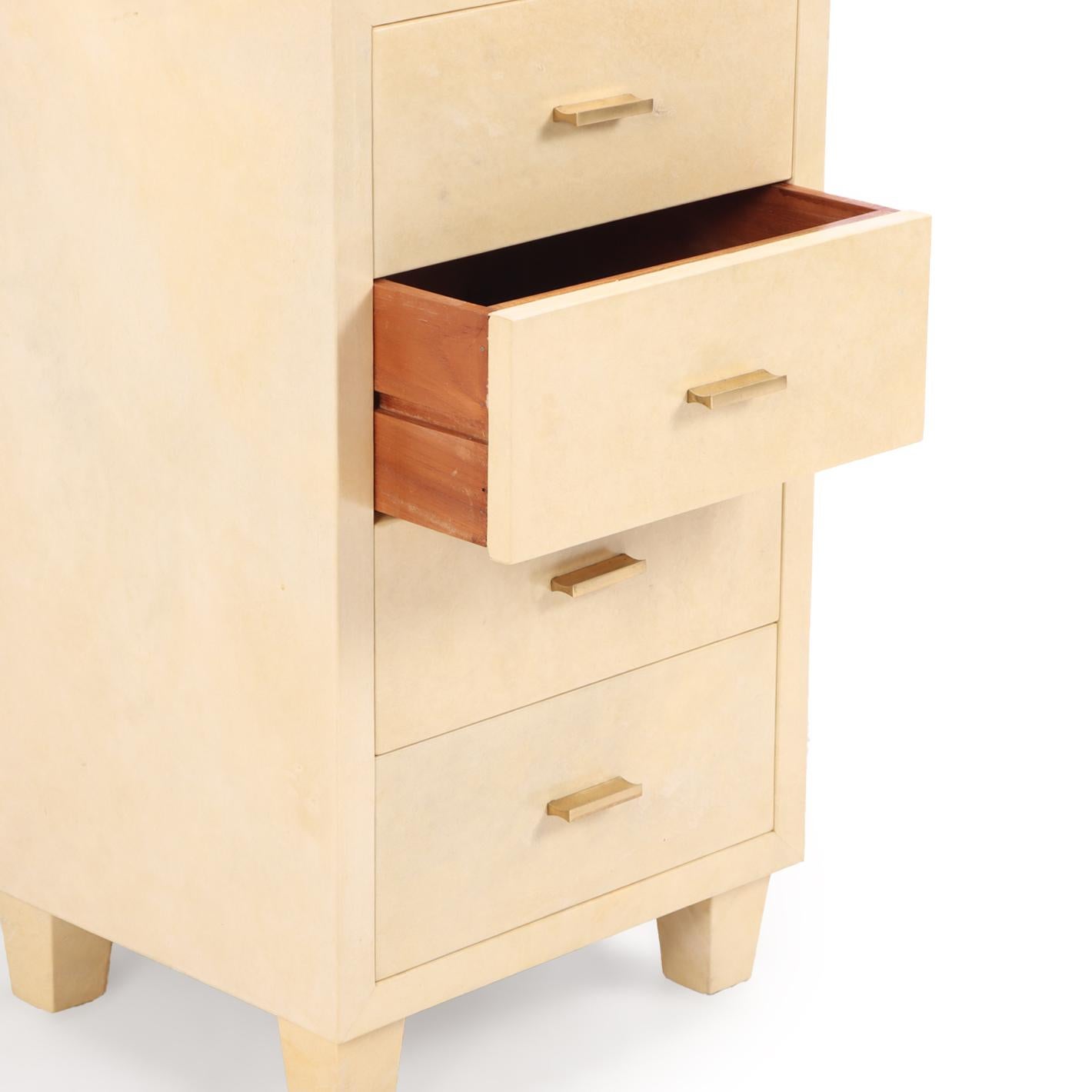 A sophisticated pair of four-drawer cabinets or nightstands, circa 1960, wrapped in richly toned natural parchment (pergamino). The clean, rectilinear forms are complemented by minimal brass hardware and short square tapering legs, allowing the