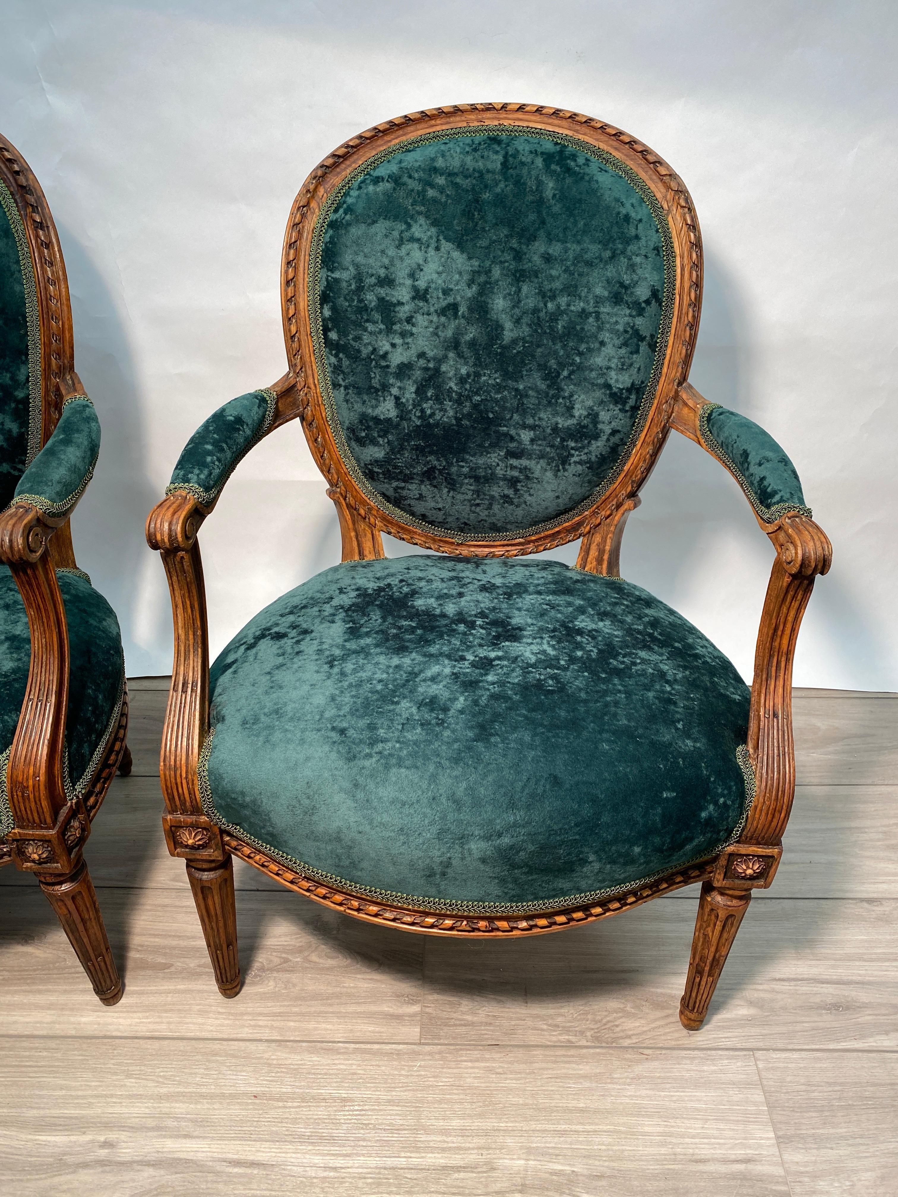 This is a rare pair of period Louis XVI fauteuil arm chairs in solid walnut. Recently upholstered in crushed emerald green fabric. Recently waxed finish and re-upholstered. 

Measures: 34.5