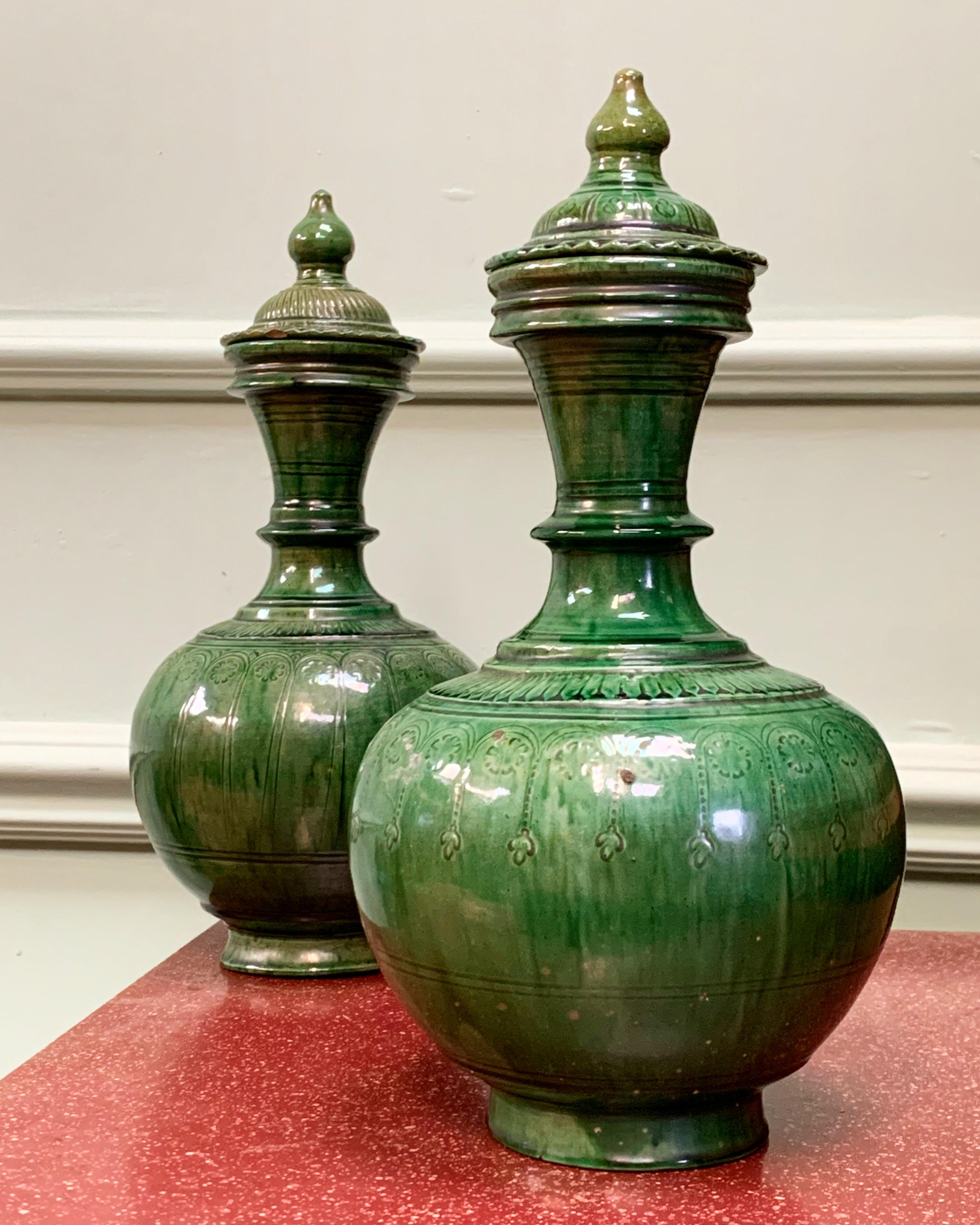 A pair of vases with rounded body, widening tubular neck and mouth, the body with moulded under the plan green glaze with a band of arched floral motifs around the shoulder and slight iridescence of glaze all over. Derived from the green glazed
