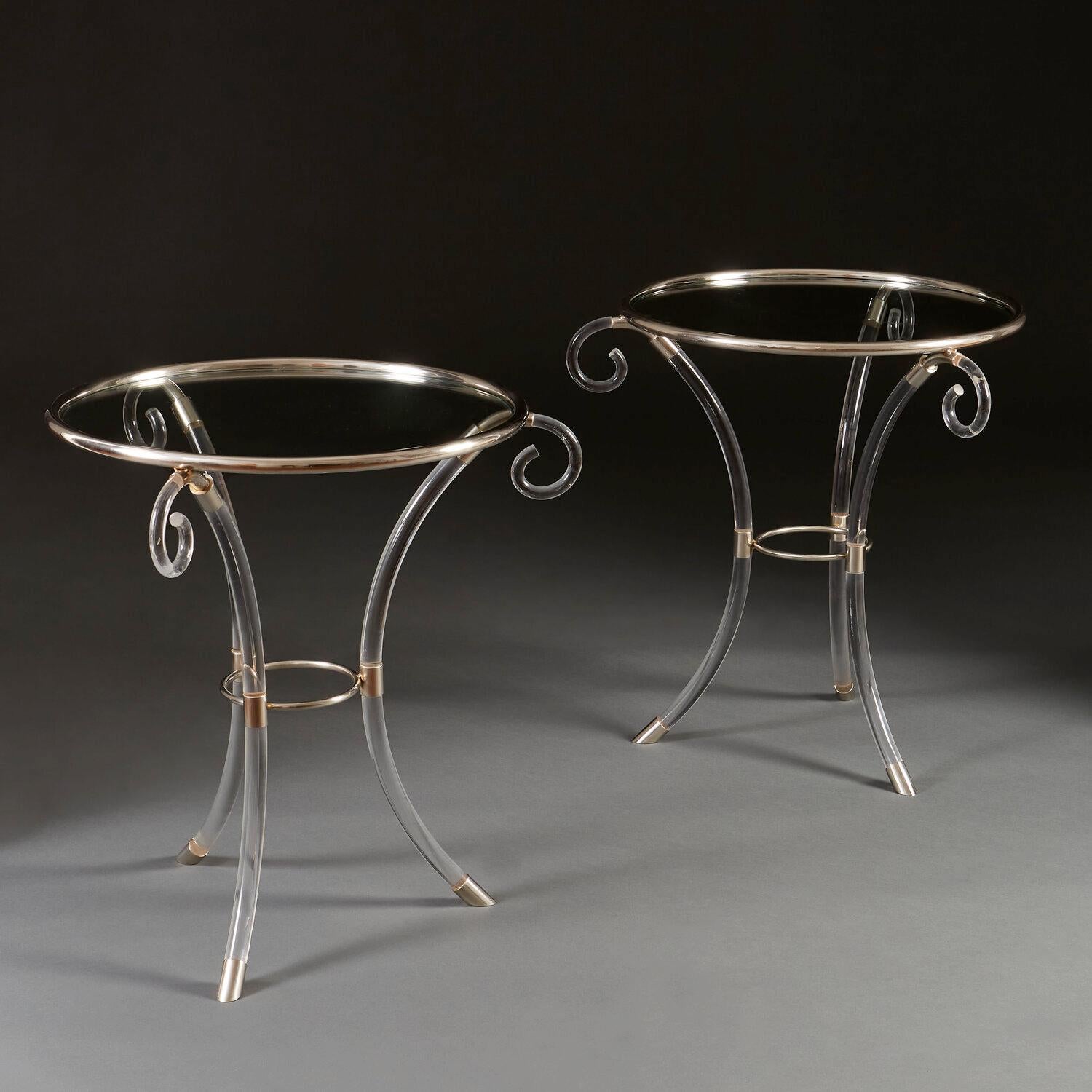 A pair of Perspex circular occasional tables with brass banding, the tripod base with sabre legs surmounted by scrolls, and terminating in brass sabots.