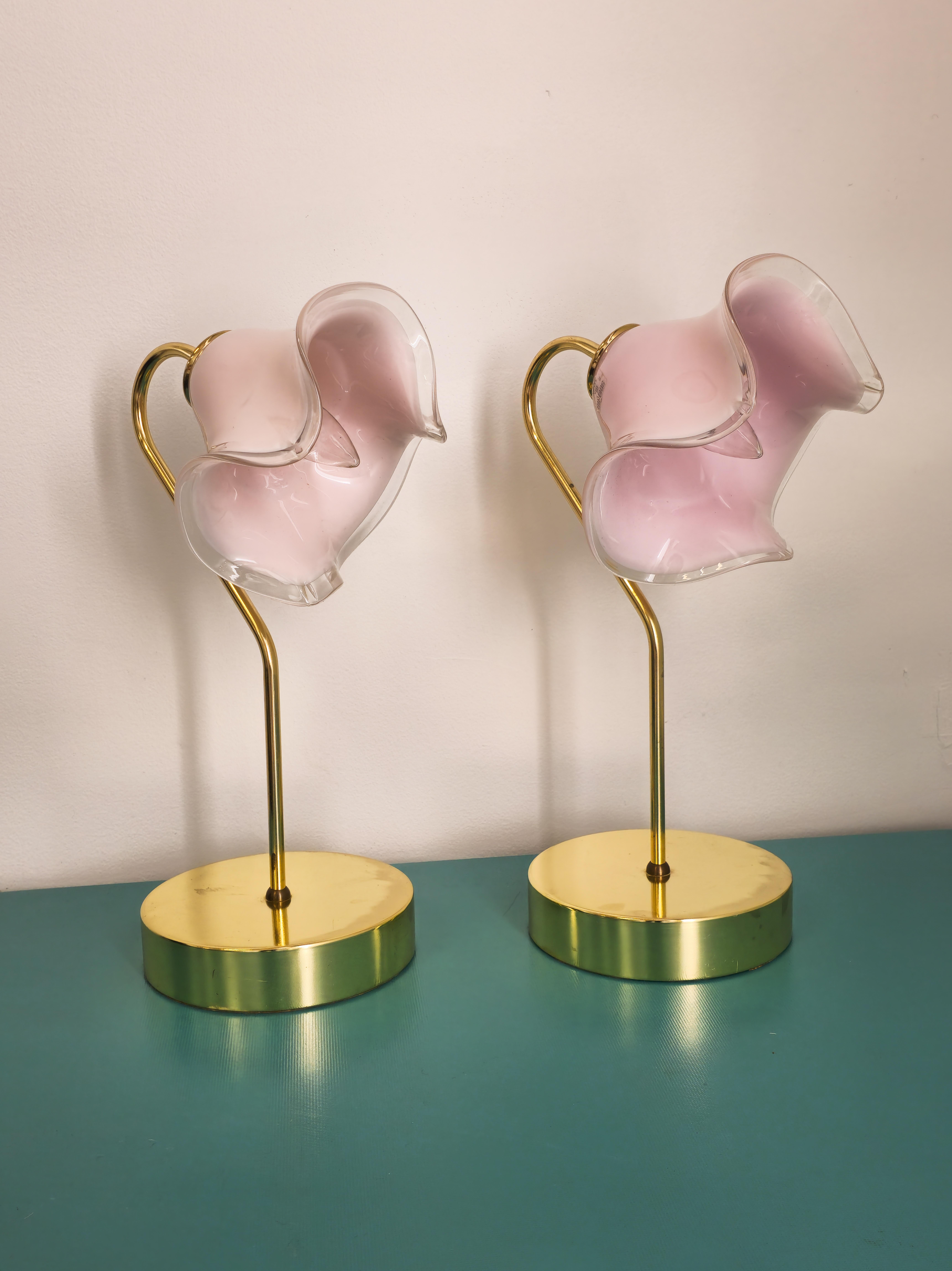 Stunning pair of pink murano art glass and brass table lamps. The beautiful art glass is made pink murano art glass. The shape of the glass shade resembles a floral form. The body of the lamps are brass. It's brass body is curved at the top where it