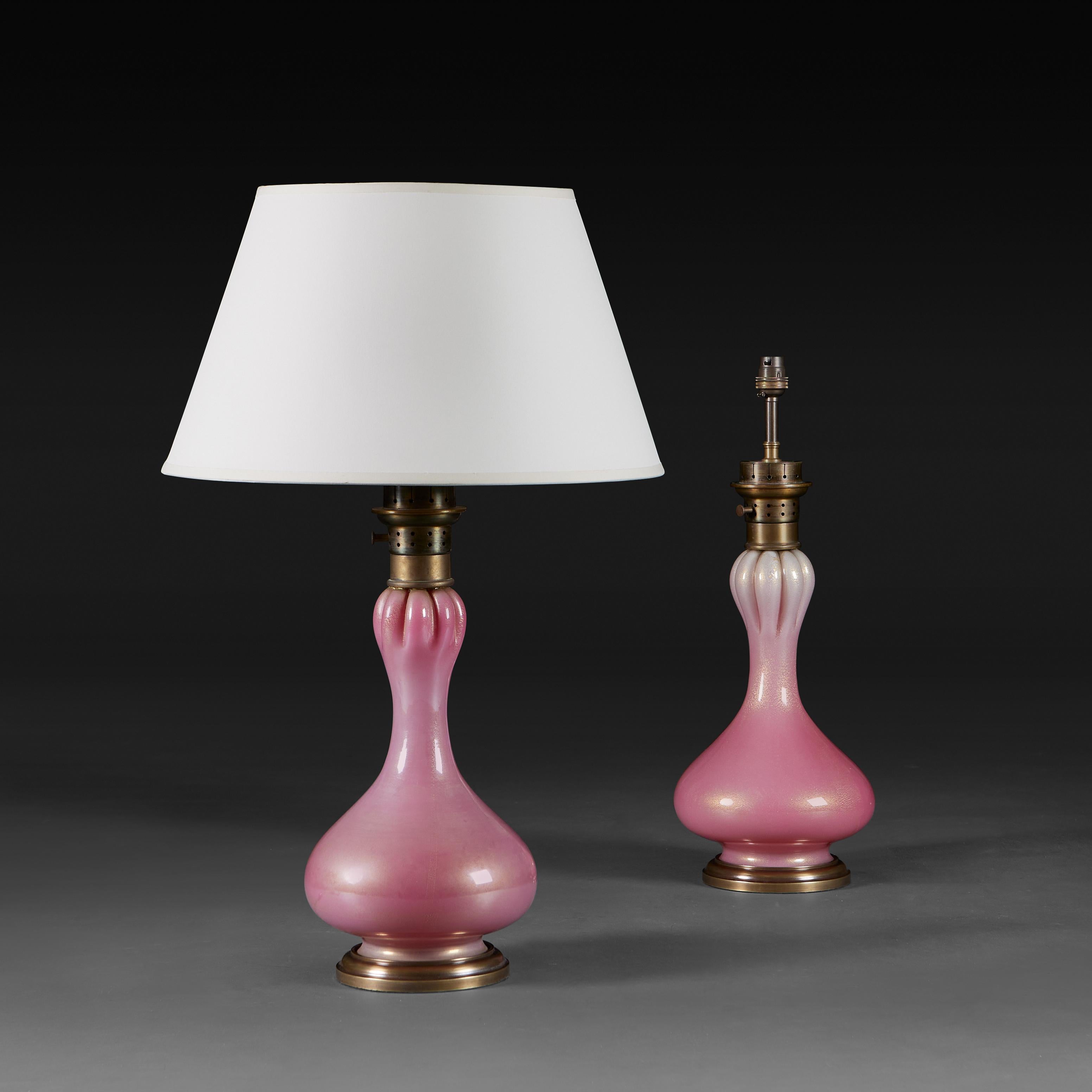 Italy, circa 1950 

A pair of pink Murano glass lamps of bulbous bottle form with gold aaventurina throughout, the necks ribbed and mounted with pierced brass collars and the glass supported on patinated brass bases.

Height 41.00cm
Diameter of base