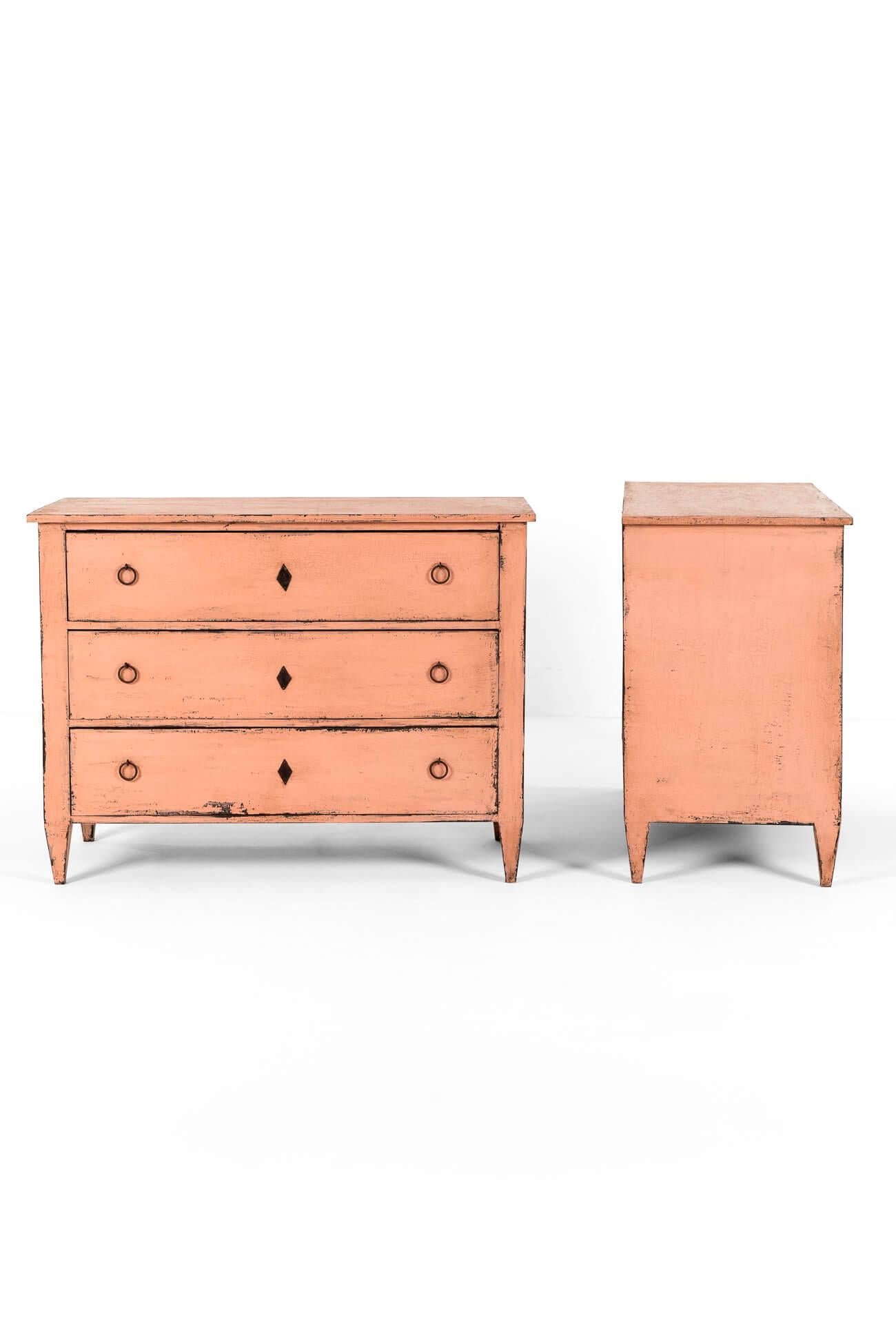 Una splendida coppia di ampi commodes del XIX secolo con finitura rosa blush.

Ogni mobile ha uno spesso piano in Oak e una struttura in pino con tre cassetti graduati e scorrevoli.

Ogni cassetto è completato da tiretti ad anello in ferro e finte