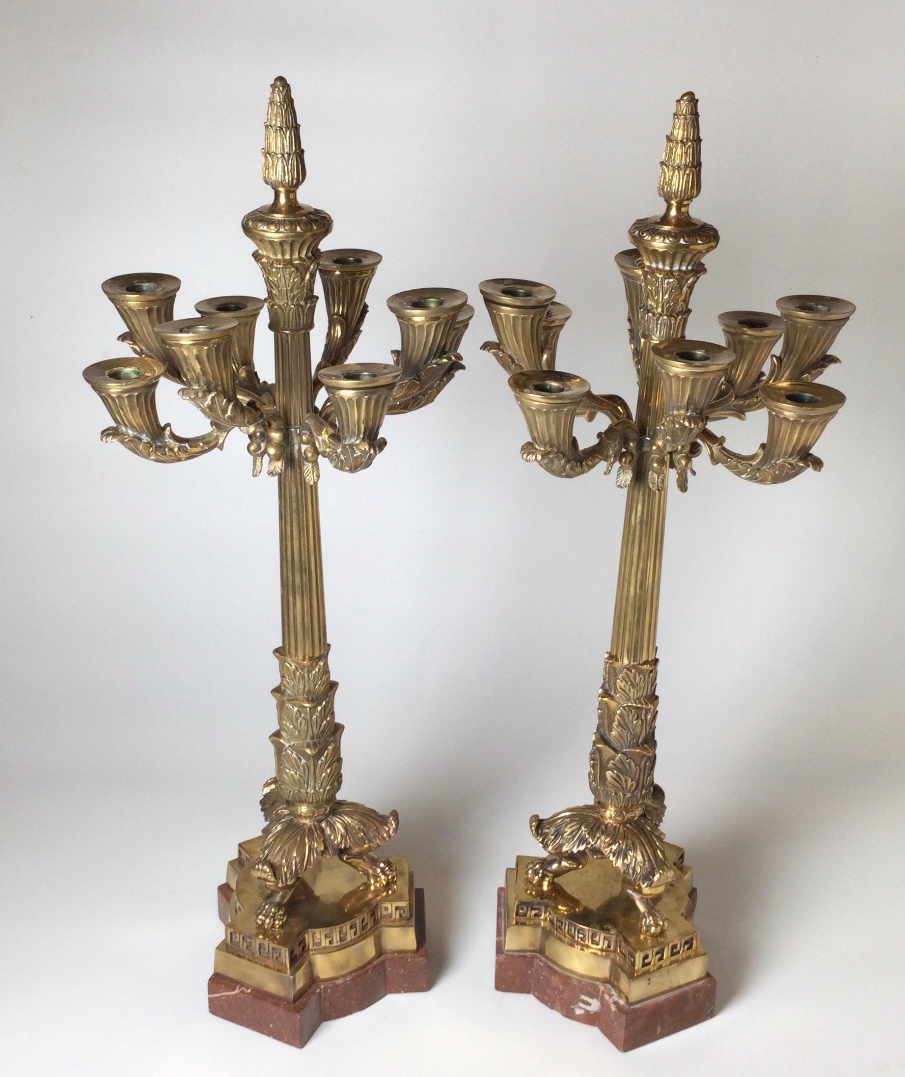 A pair of 8 arm polished bronze Charles X style candelabra with rouge marble bases. The cast arms and center column with tripod paw feet on marble base. One arm has been reattached.
