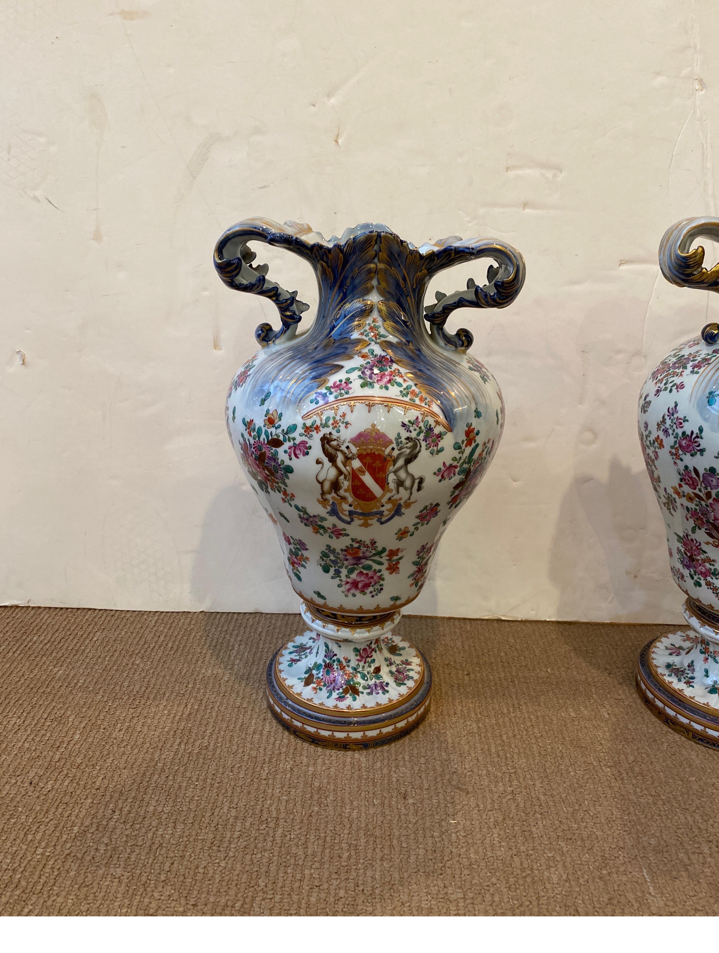 A pair of hand painted porcelain with armorial cartouches on the fronts and bouquets of flowers on the backs. The shapely form with cobalt and hand gilt decoration, marked with the N with crown mark in blue, under-glaze.