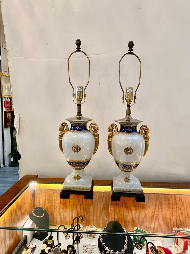 A Pair of elegant hand painted neoclassical porcelain lamps. The bulbous form with cobalt and gold decoration with gilt female form handles. The shades are for photographic purposes only and not included. The height when paired with a shade is 28