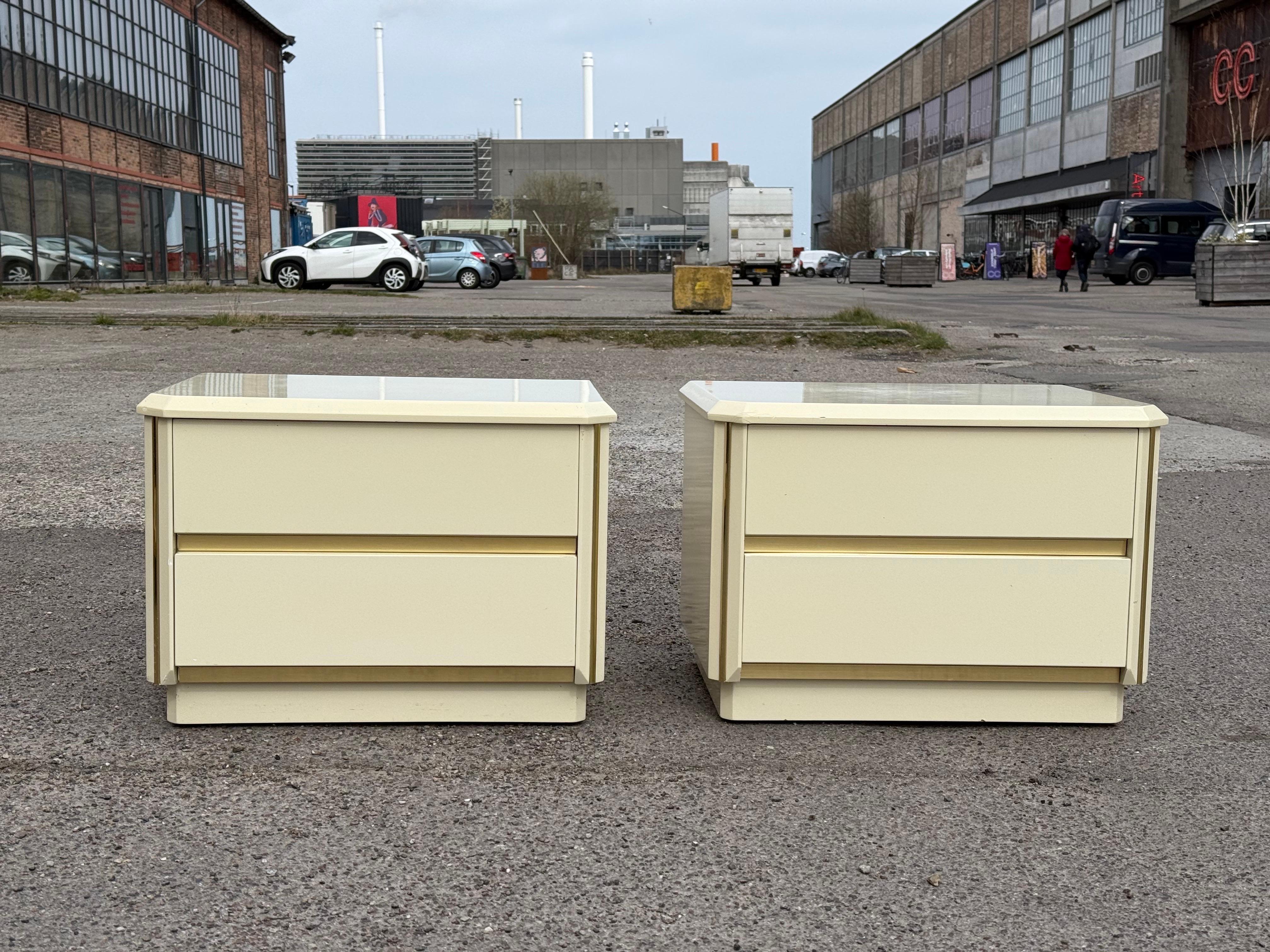 Stunning pair of Italian Postmodern 1980s cream lacquer laminate nightstands, accented with subtle gold details. Designed to blend functionality with sophisticated charm, each piece offers ample storage with two spacious drawers, perfect for keeping