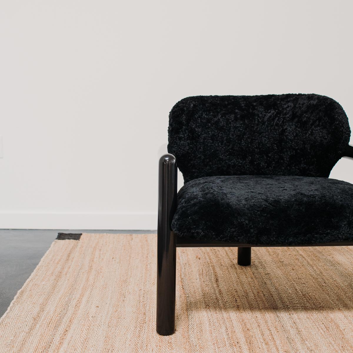 A pair of three legged armchairs chairs restored and reupholstered by the Selby House in a black Skandilock shearling.
