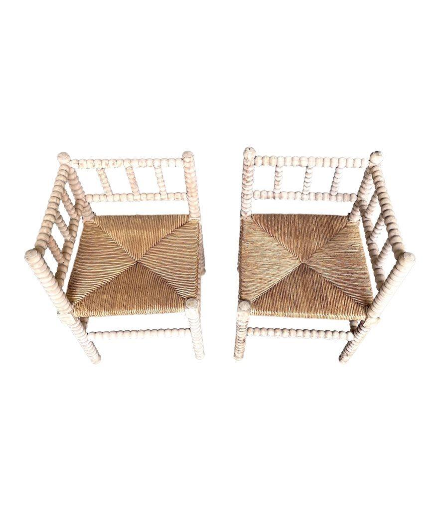 A pair of provincial French, hand carved bleached oak bobbin corner chairs with hand woven rush seats.