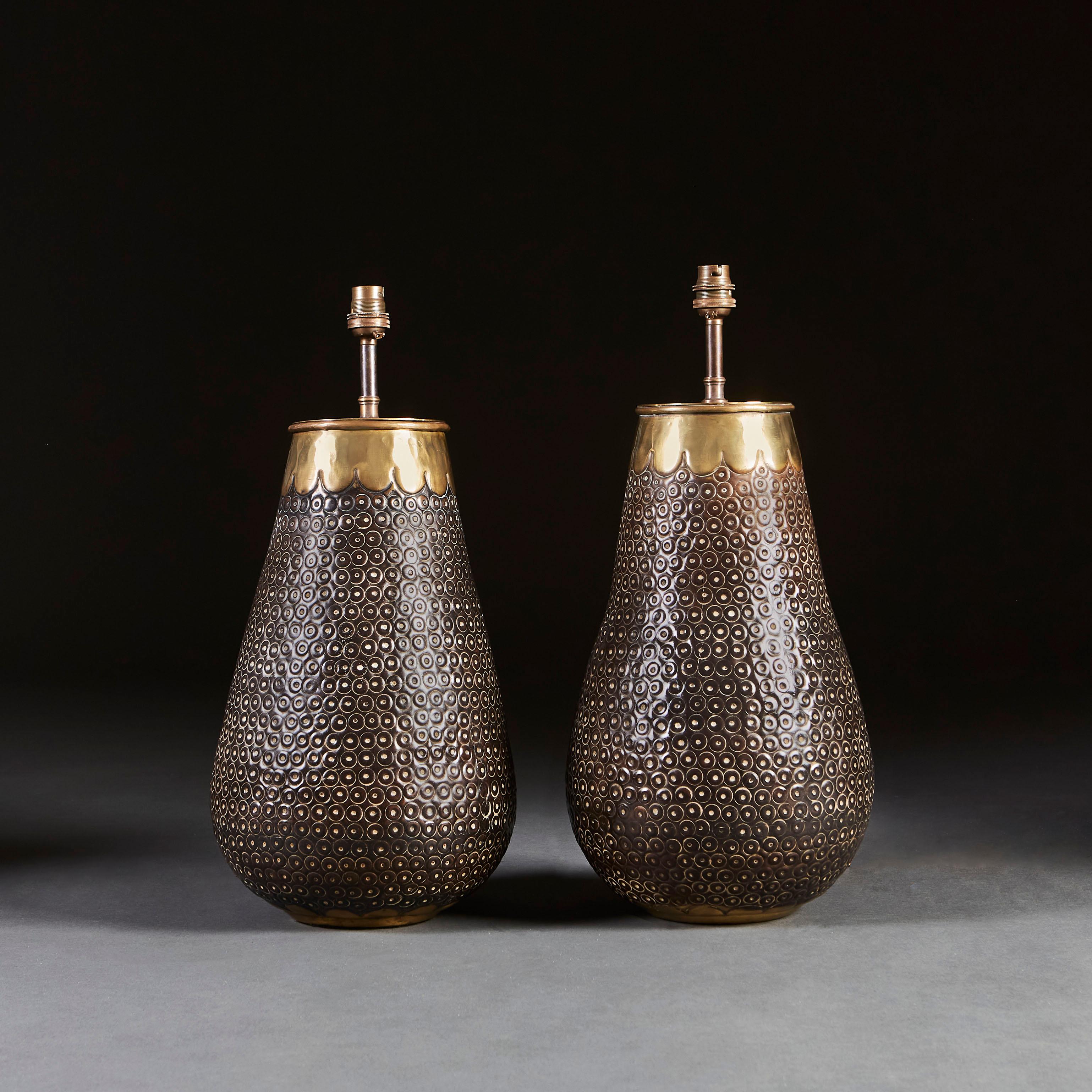 A pair of puched dark metal lamps of baluster form, the rims with contrasting brass bands with scallop edge.