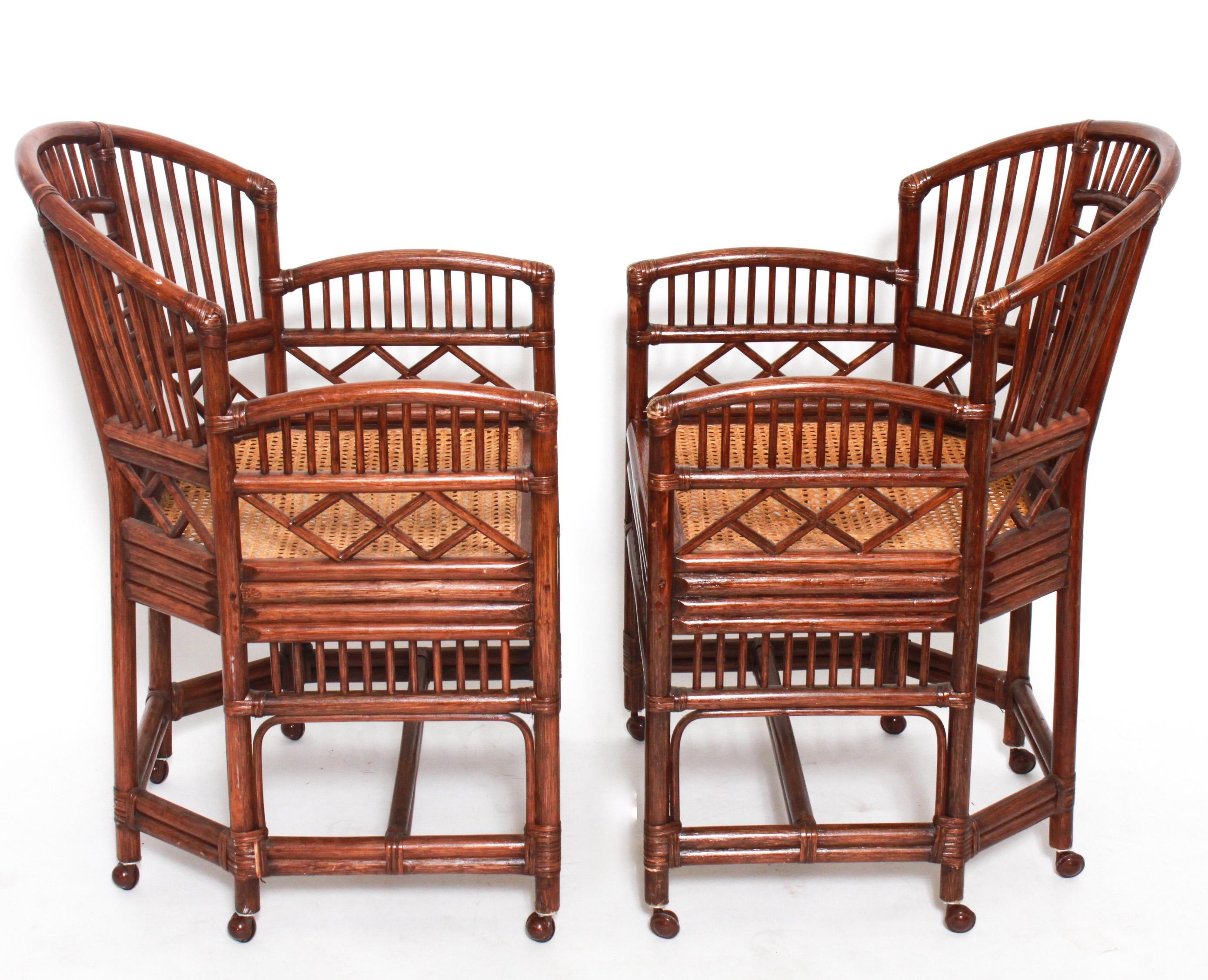 A pair of rattan chinoiserie fretwork armchairs with caned seats and casters to the feet.