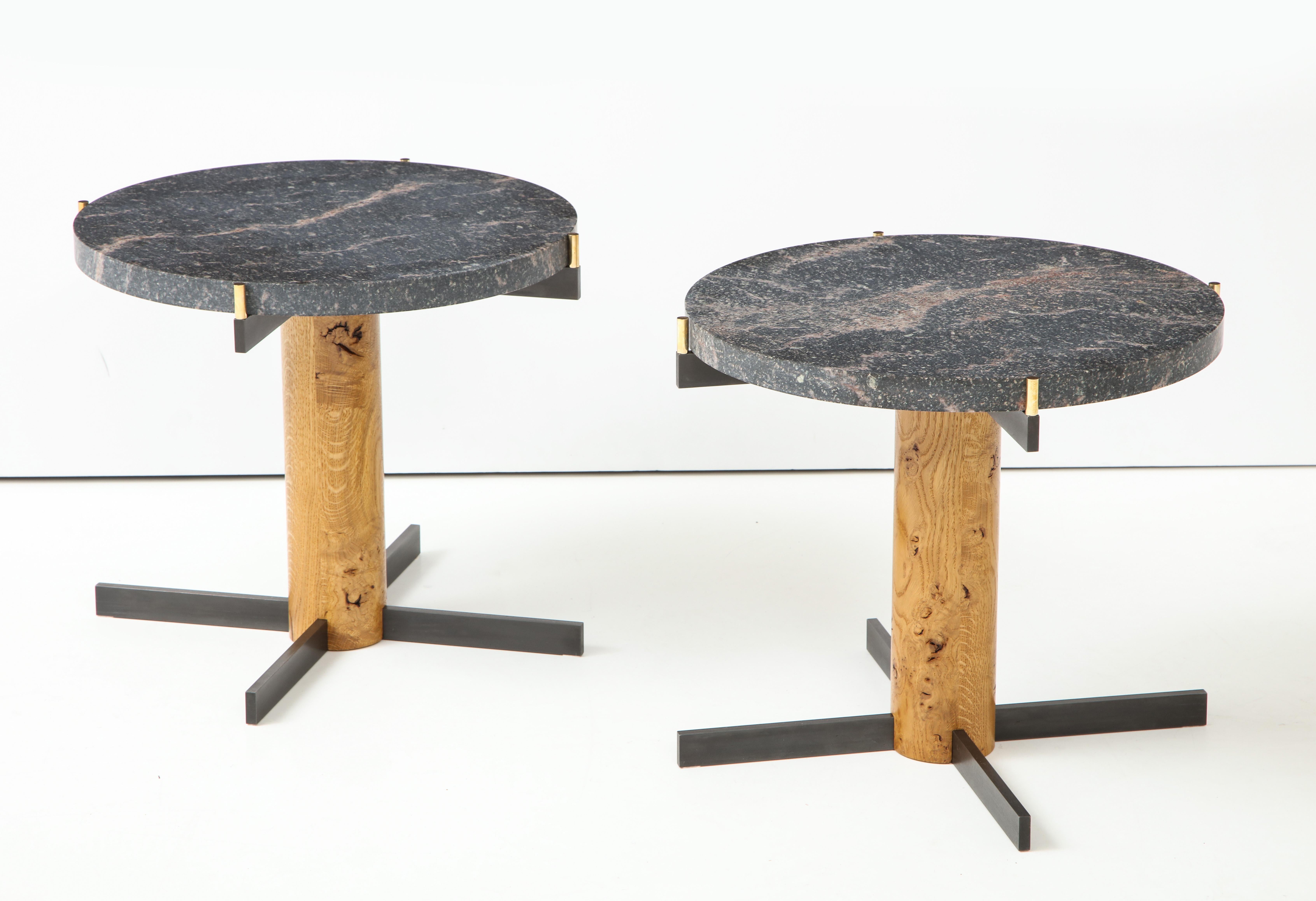 A pair of Danish side tables, designed by Rune Bruun Johansen, Copenhagen, circa 2000s. Each table with a thick circular Nero Marquina marble top supported by a iron cross bar with polished brass lugs, raised on a circular European oak stem and