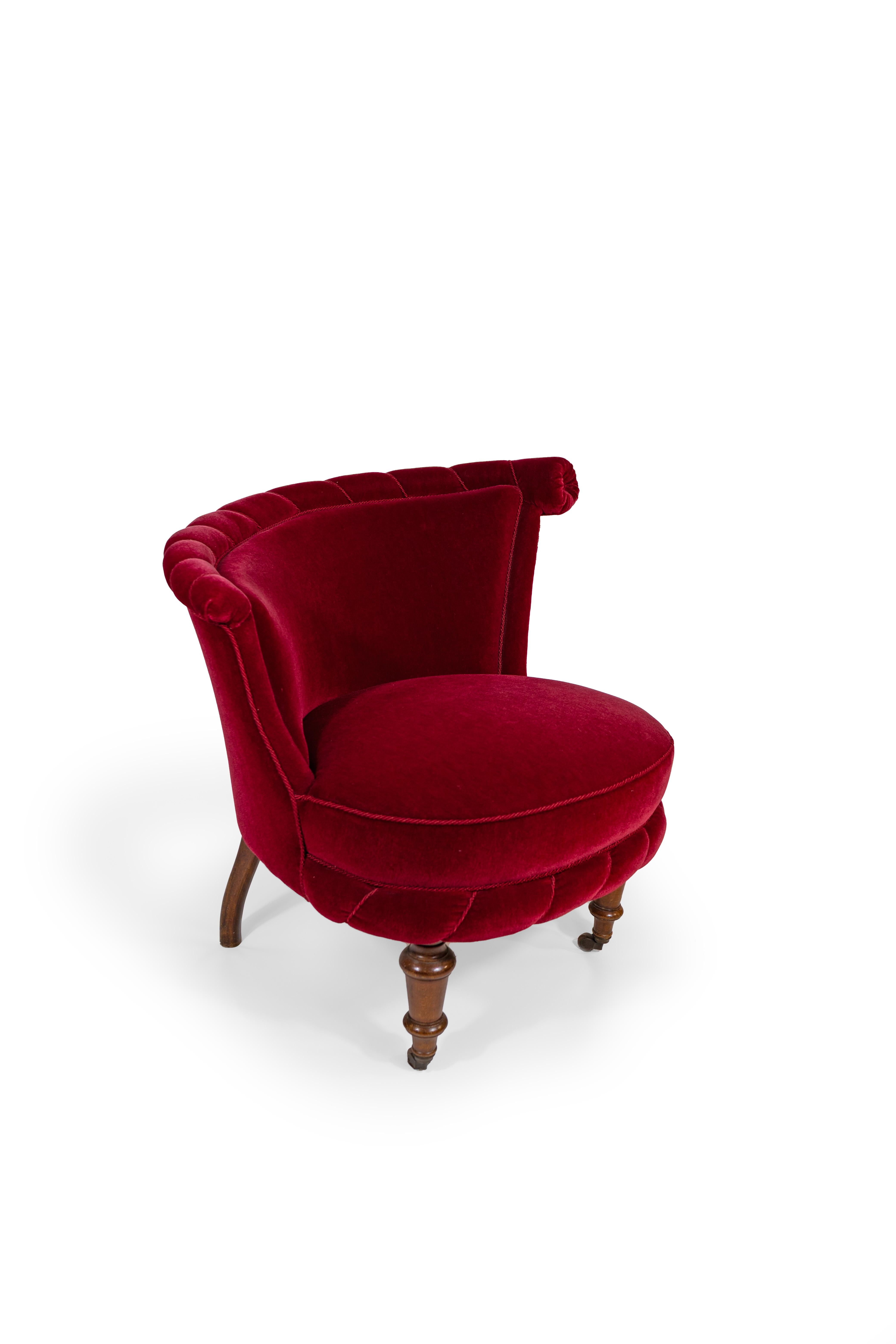 A pair of slipper chairs, vintage upholstery in garnet red velvet in very good condition. These chairs feature low, curved backs with rolled tops, accented by vertical channel stitching and a central rosette detail. The rounded seats are generously
