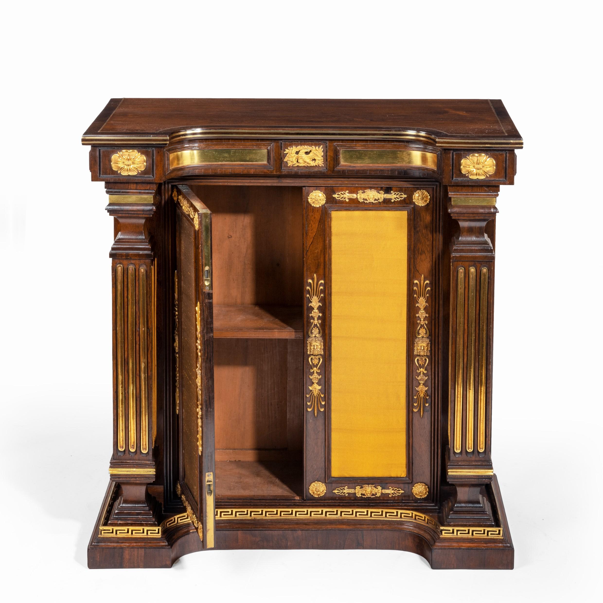 A pair of Regency brass-inlaid rosewood side cabinets, each of rectangular form with a concave frieze concealing a button to open a pair of glazed with doors re-lined in yellow silk enclosing a single adjustable shelf, flanked by square-section