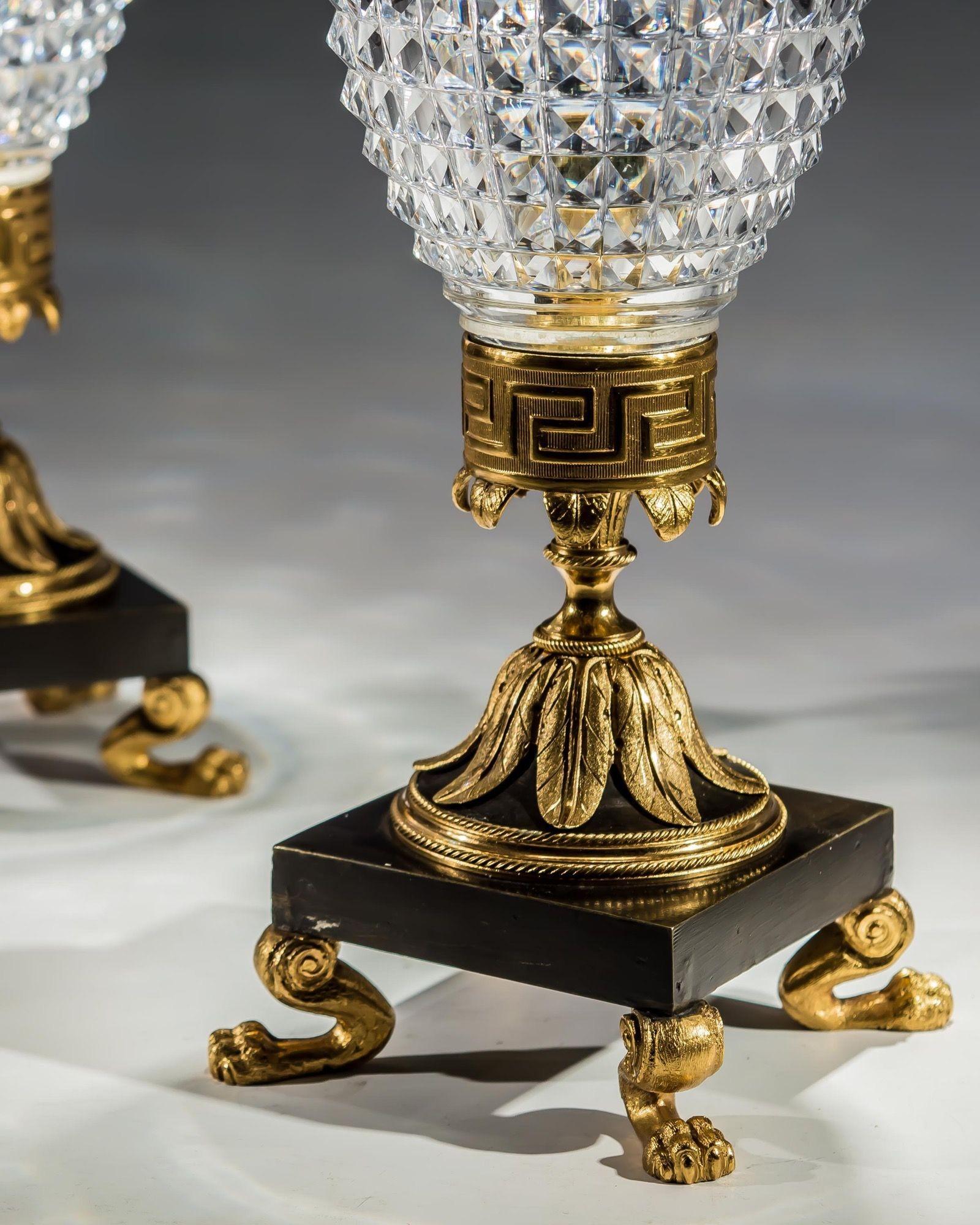 A fine pair of Regency storm lights with elaborately cut square diamond shades of bullet form, mounted on an ornate square, ormolu and bronze base with key pattern mount on foliate socle, all supported upon lion paw feet.