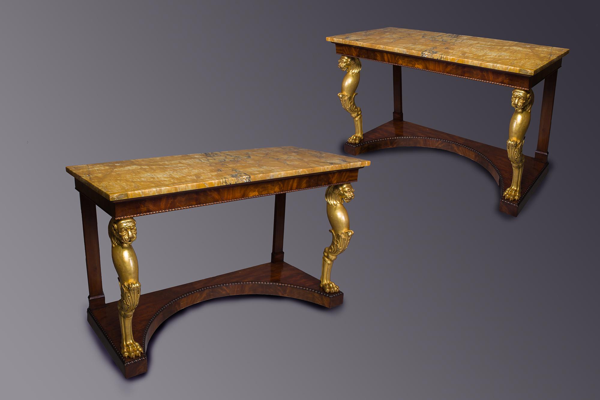 A Fine Pair of Regency Gilt-wood and mahogany console tables
The Original rectangular Sienna marble tops, above a moulded lip,
above a flamed mahogany veneered frieze, with a beaded moulding, 
resting on carved gilt-wood Lion monopodia legs with