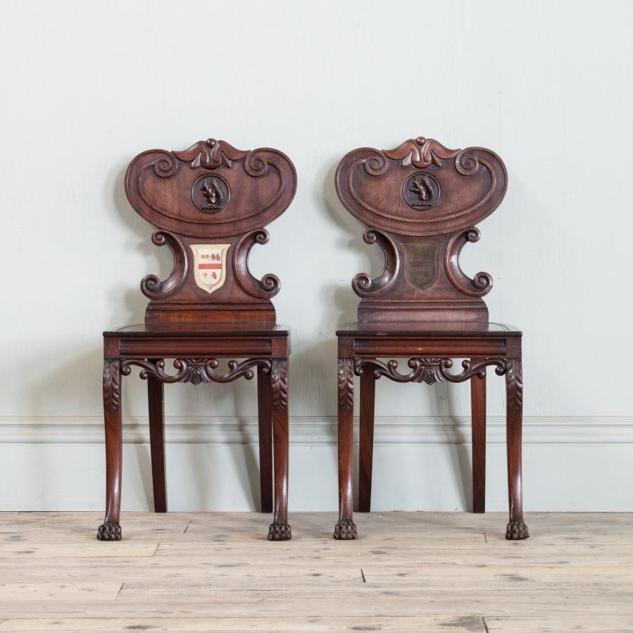 A pair of Regency mahogany armorial hall chairs, with unusual carved squirrel details and painted shields.