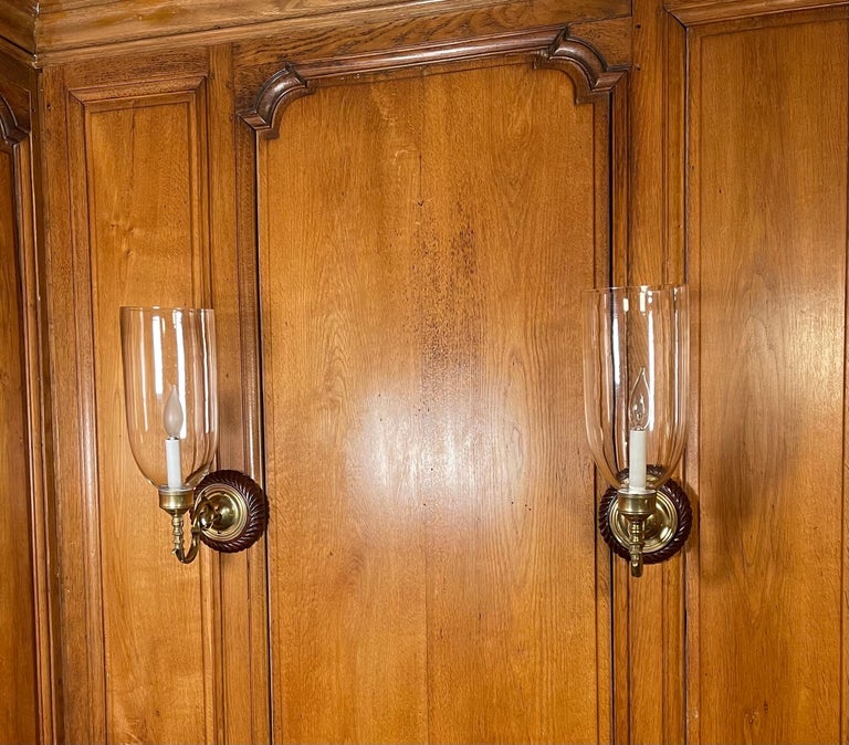 A pair of antique hand-carved Plaques from mahogany Regency backplates, patinated brass sconce fittings, and hand-blown clear shades. Newly Electrified with one candelabra-based socket per sconce.