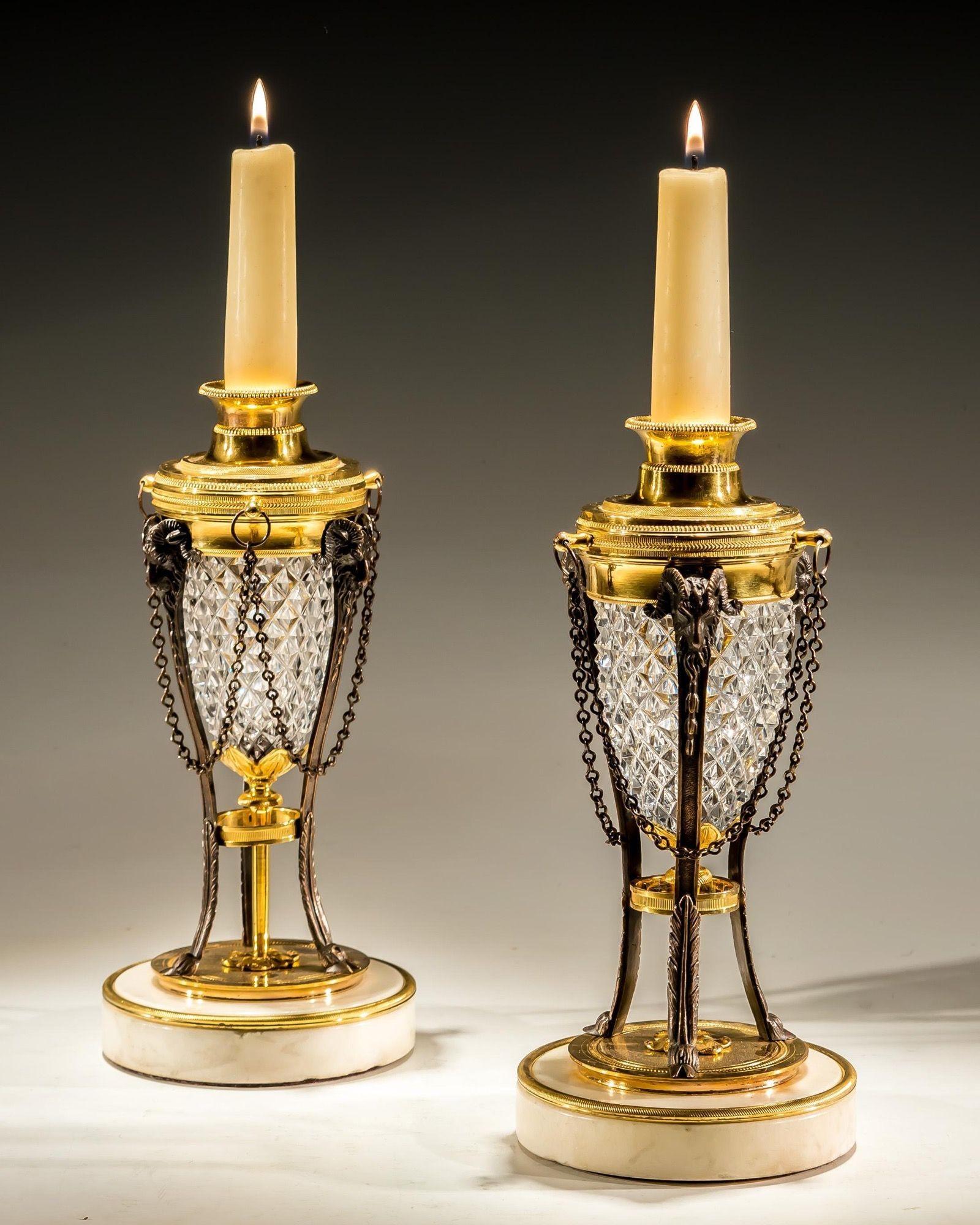 A pair of regency cassolettes on white marble bases mounted with ormolu bands, supporting three bronzed ram legs terminating with ram heads, These mounted to central ormolu band fitted with diamond cut, glass reservoir and corresponding lid with