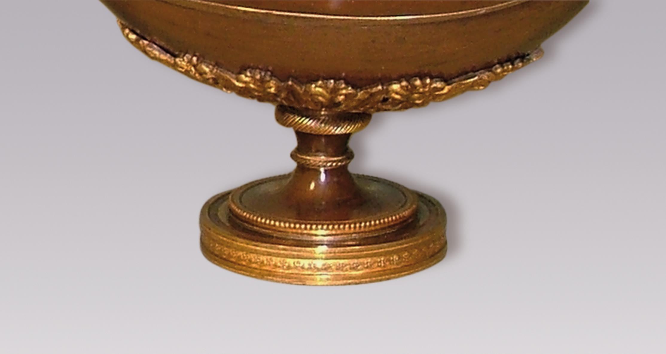 Una bella e insolita coppia di candelieri a due luci in bronzo e ormolu dell'inizio del XIX secolo, a forma di lucerna classica, con applique a fiamma e coperchi centrali con decorazione a foglie d'acanto in basso, sollevati su basi circolari