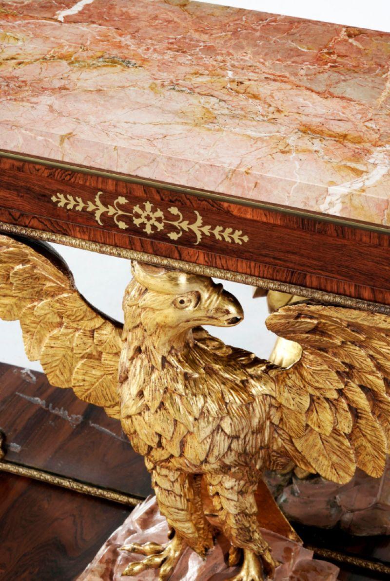 Paire de grandes consoles à aigle de style Regency, début du 20e siècle, en placage de bois de rose avec incrustations de laiton et de bois sculpté et doré, plateau en marbre rose reposant sur un aigle aux ailes déployées, la base est décorée d'une