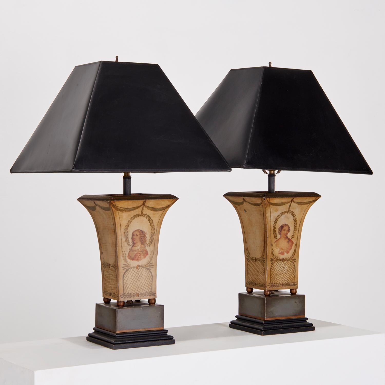 Early 20th c., a pair of Regency style tole peinte table lamps made of polychrome painted sheet metal.  Each lamp is decorated with a charming female bust and lattice borders on the facing side and with an all over cream ground. The lamps have brass