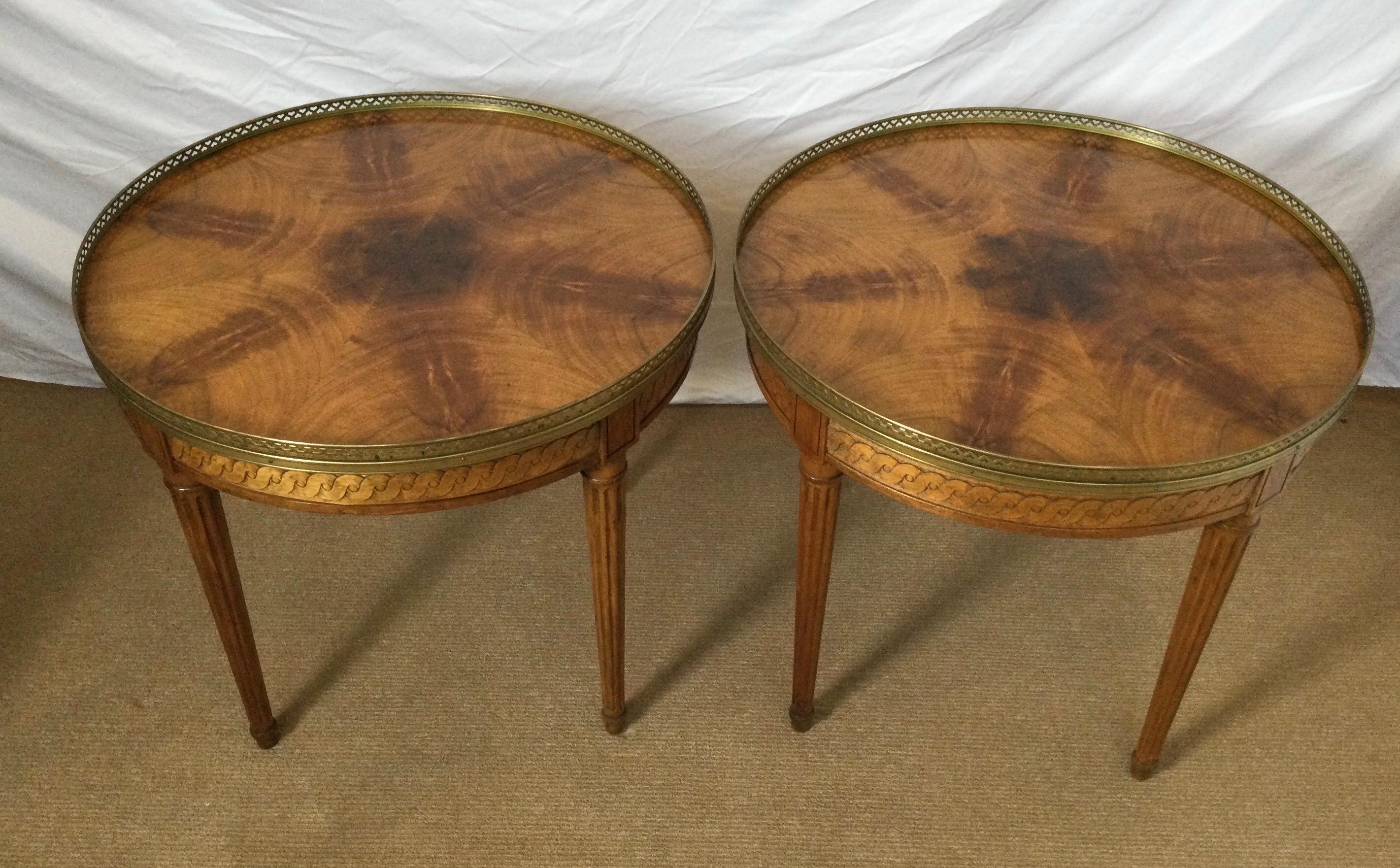 A pair of Baker Furniture round gallery edge table in a light walnut. The tops with book matched highly figurative walnut veneer with a pierced brass gallery edge with reeded louis XVI style legs.
