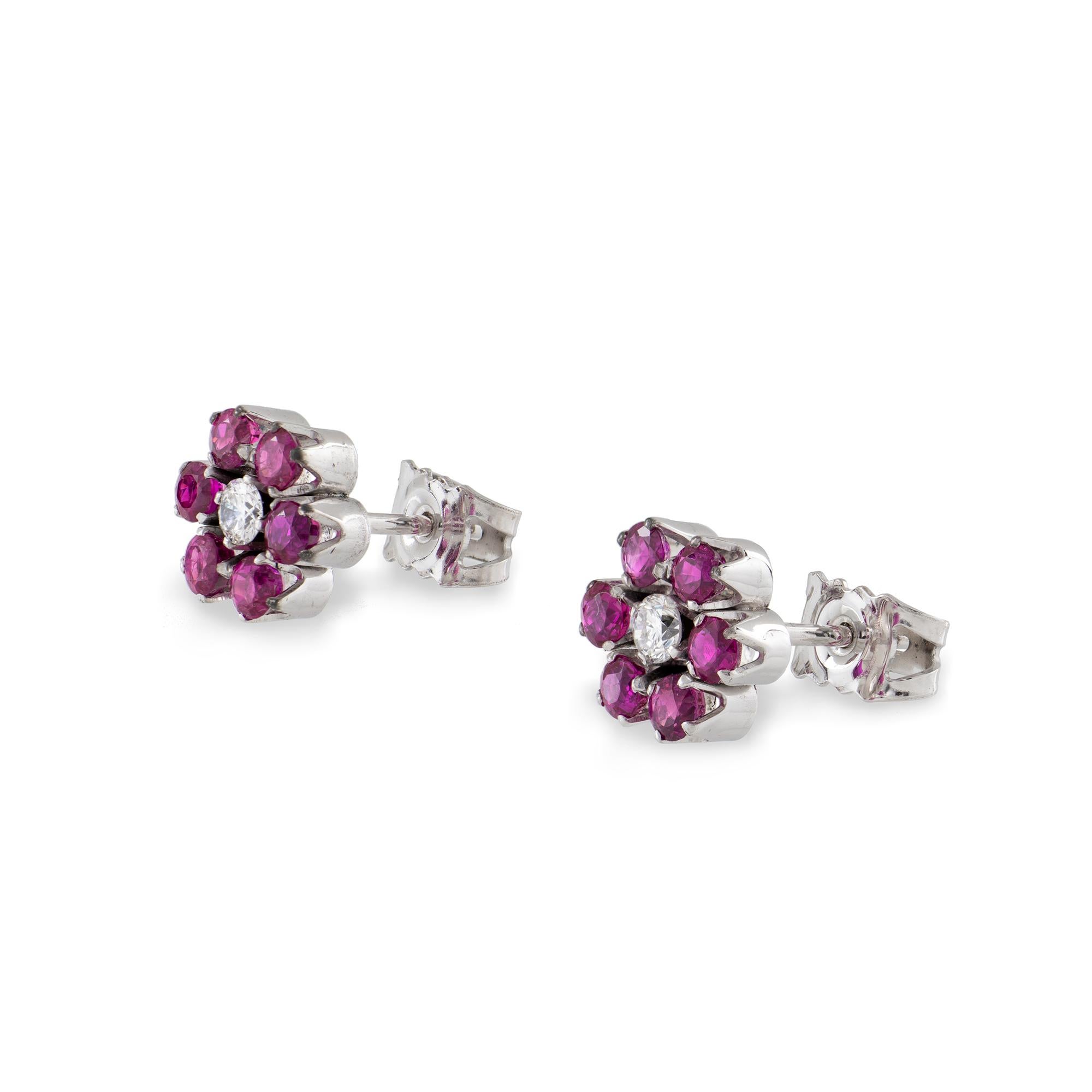 A pair of ruby and diamond floral cluster stud earrings, each set to the centre with a round brilliant cut diamond, estimated to weigh 0.20 carats in total, and surrounded by six round faceted rubies, estimated to weigh 0.80 carats in total, all